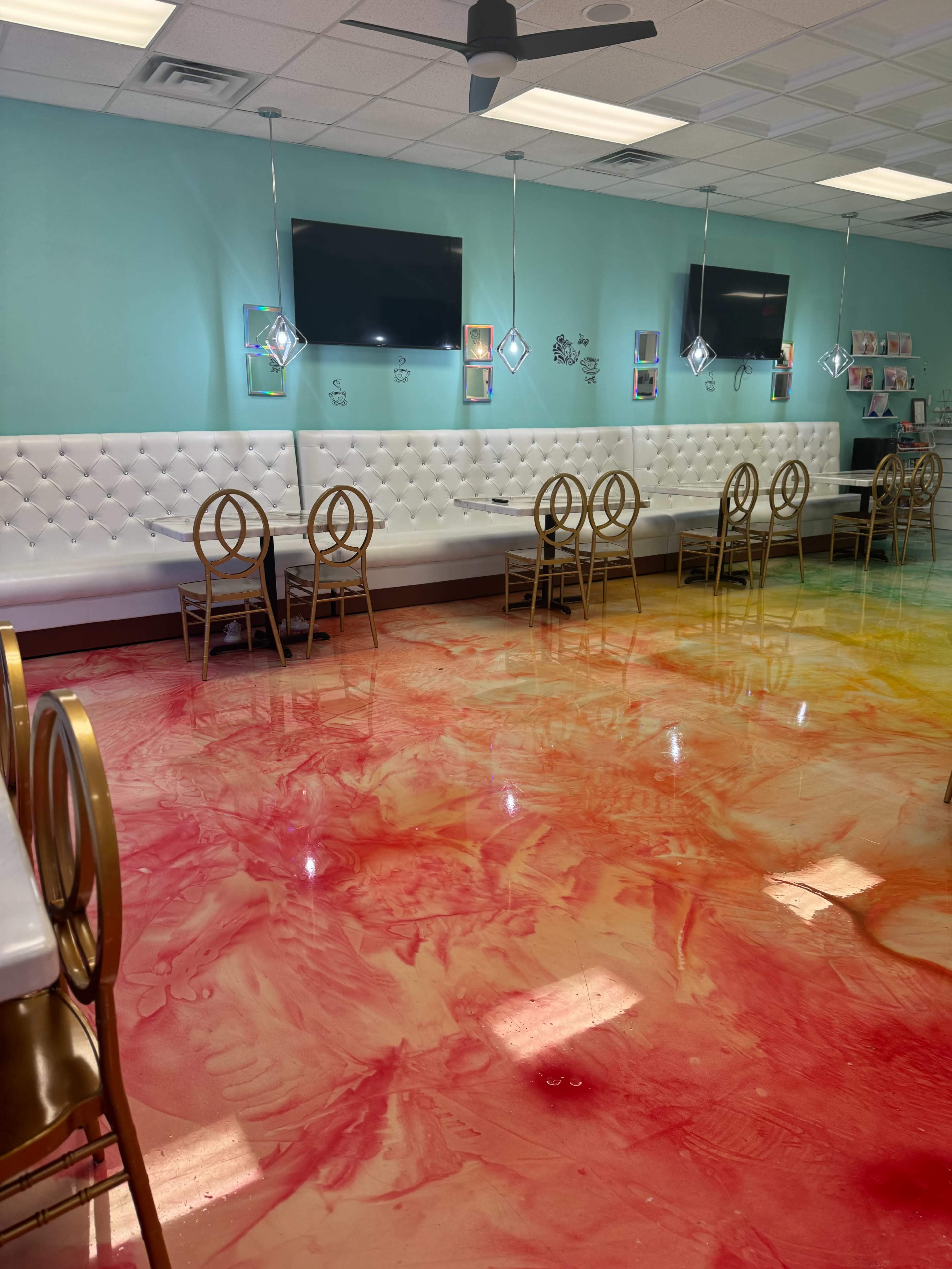 A brightly colored café interior with a shiny, marbled floor and white tufted seating against mint green walls, complemented by modern lighting fixtures.