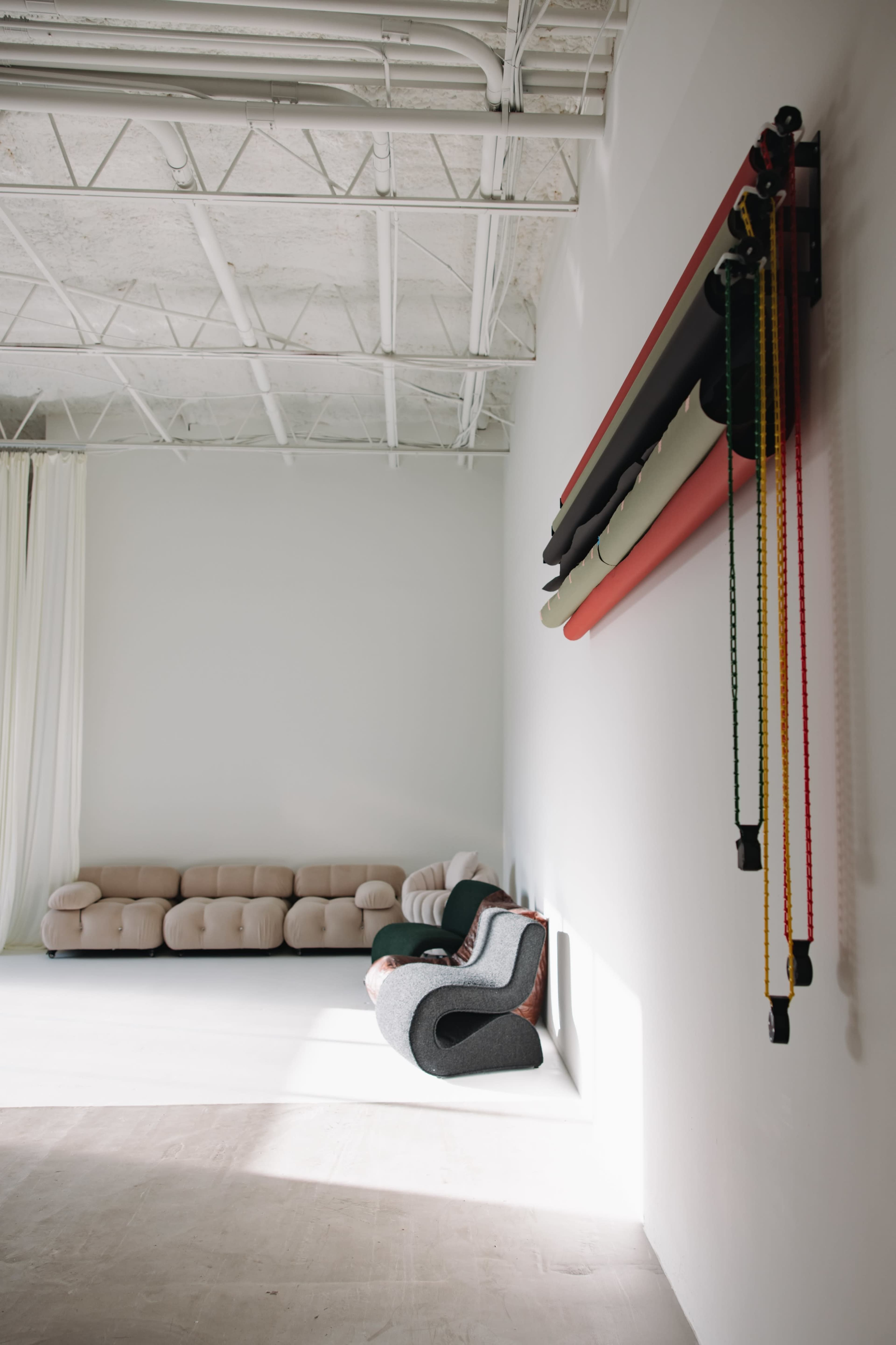 A spacious interior features a minimalist couch arranged against a light-colored wall, with colorful rolled materials hanging nearby.