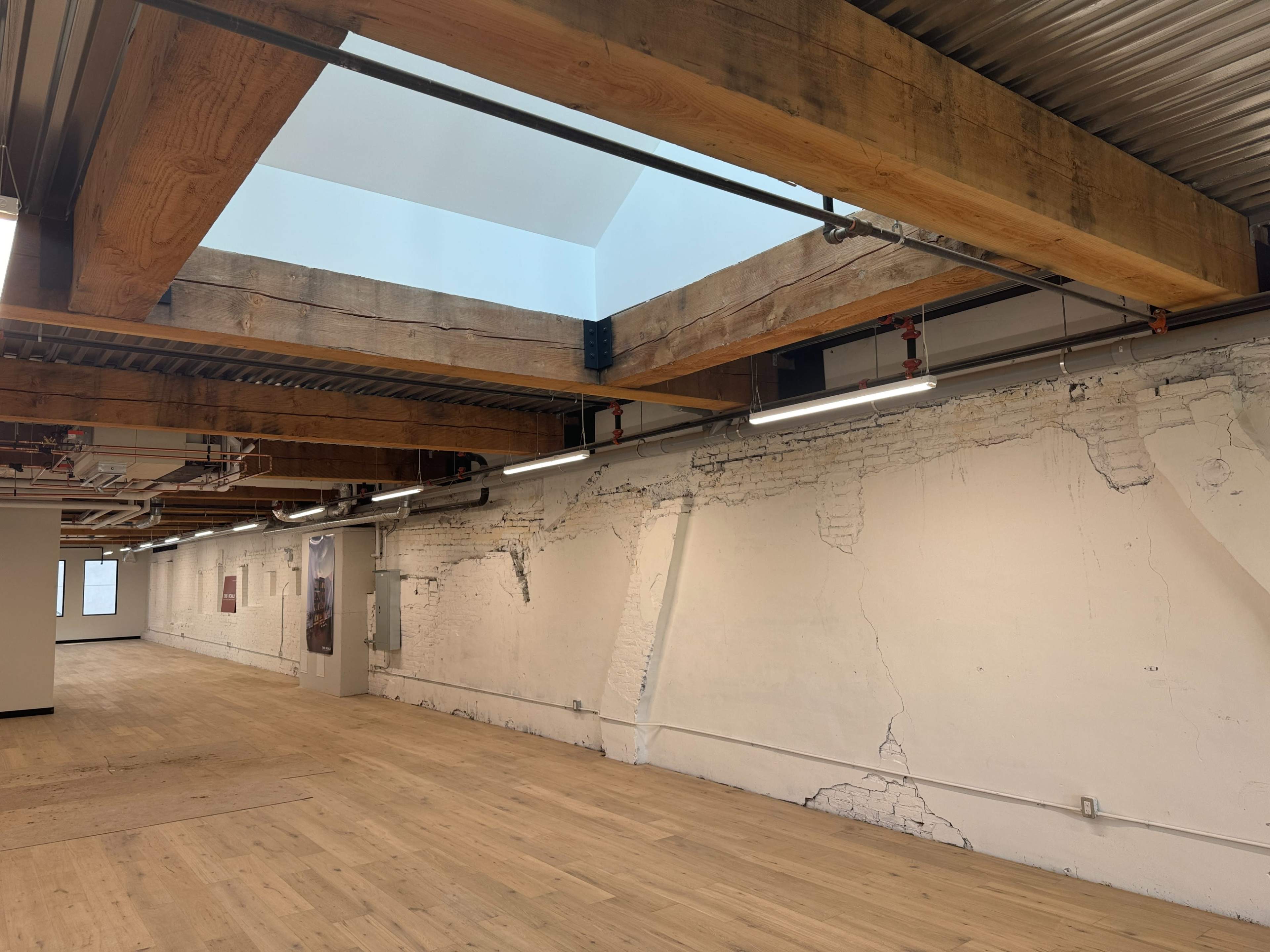 An empty interior space featuring exposed wooden beams, a skylight, and cracked white walls.