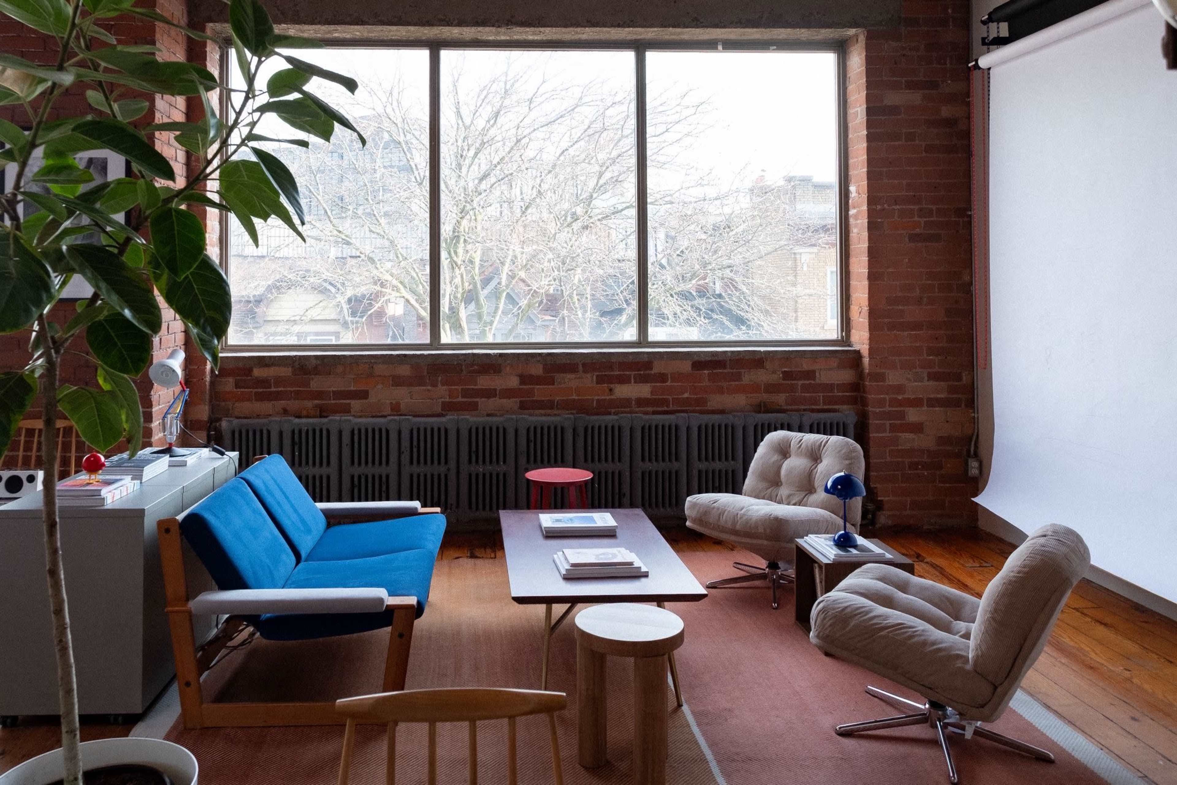 The image shows a modern living space with a blue sofa, two beige armchairs, a wooden coffee table, and large windows revealing a view of trees outside.