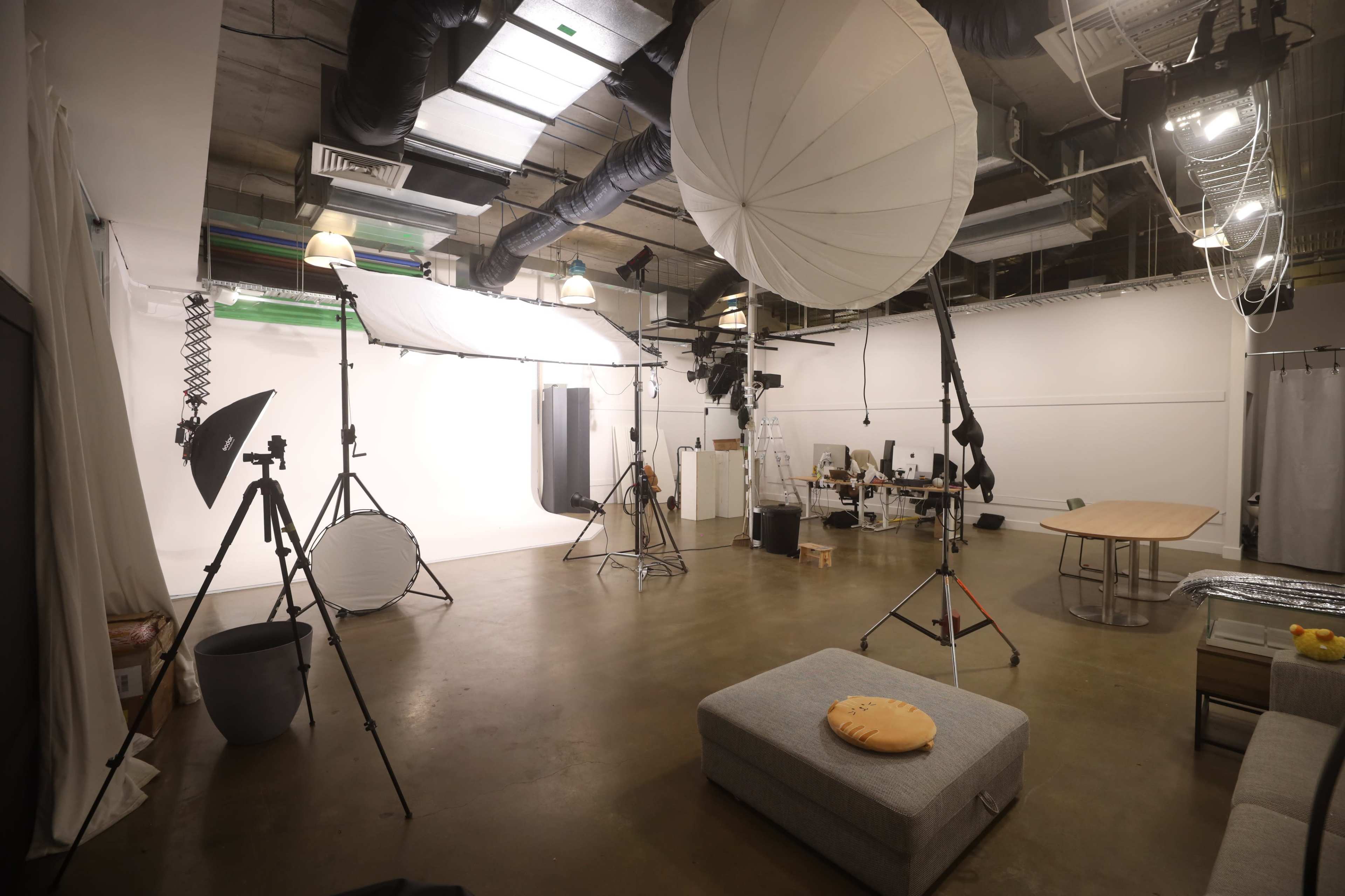 The image shows a photo studio equipped with various lighting equipment, backdrop supports, and a seating area.