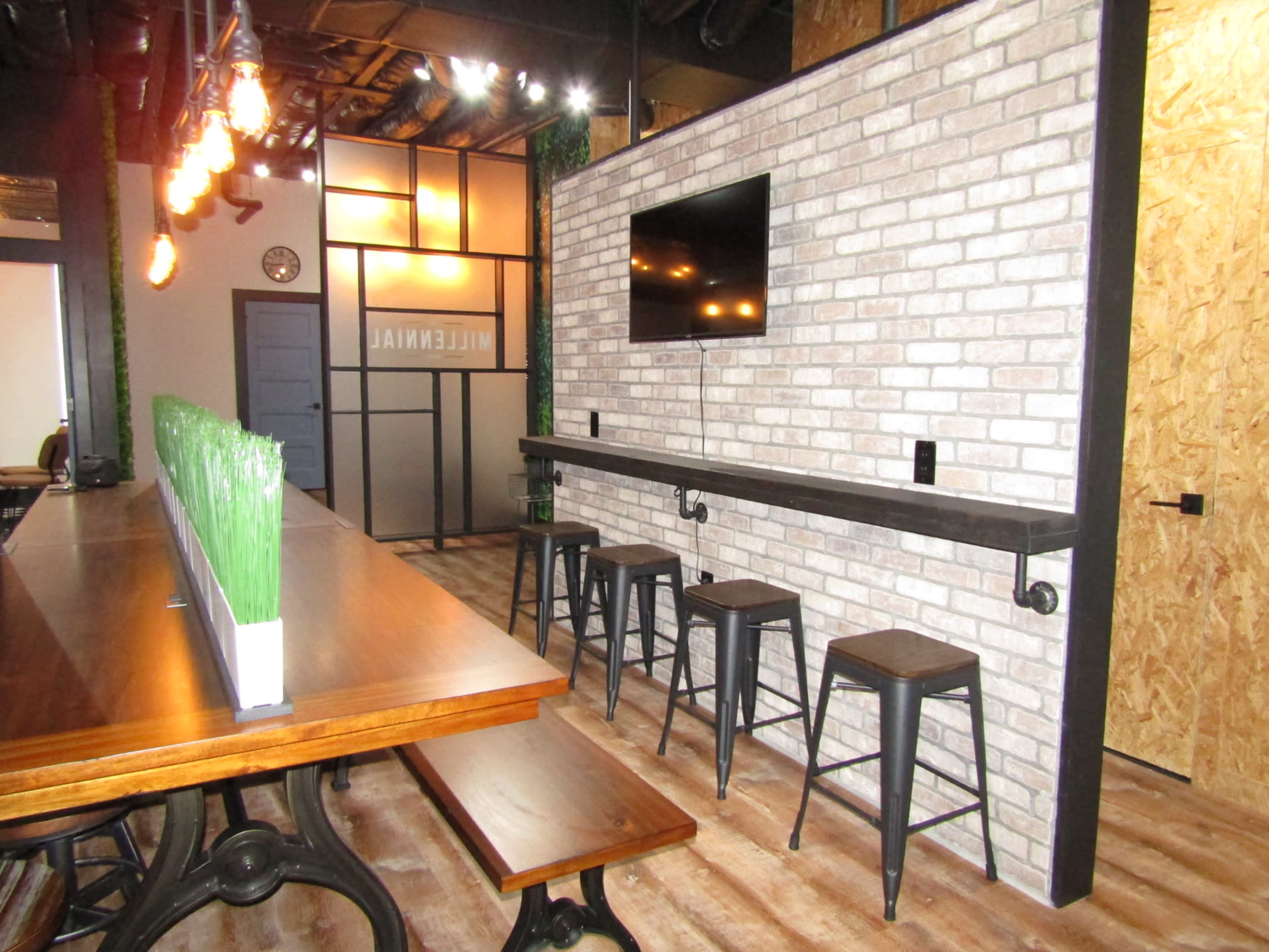 A trendy dining area featuring a brick accent wall, high stools along a bar counter, and a wall-mounted TV in a modern setting.