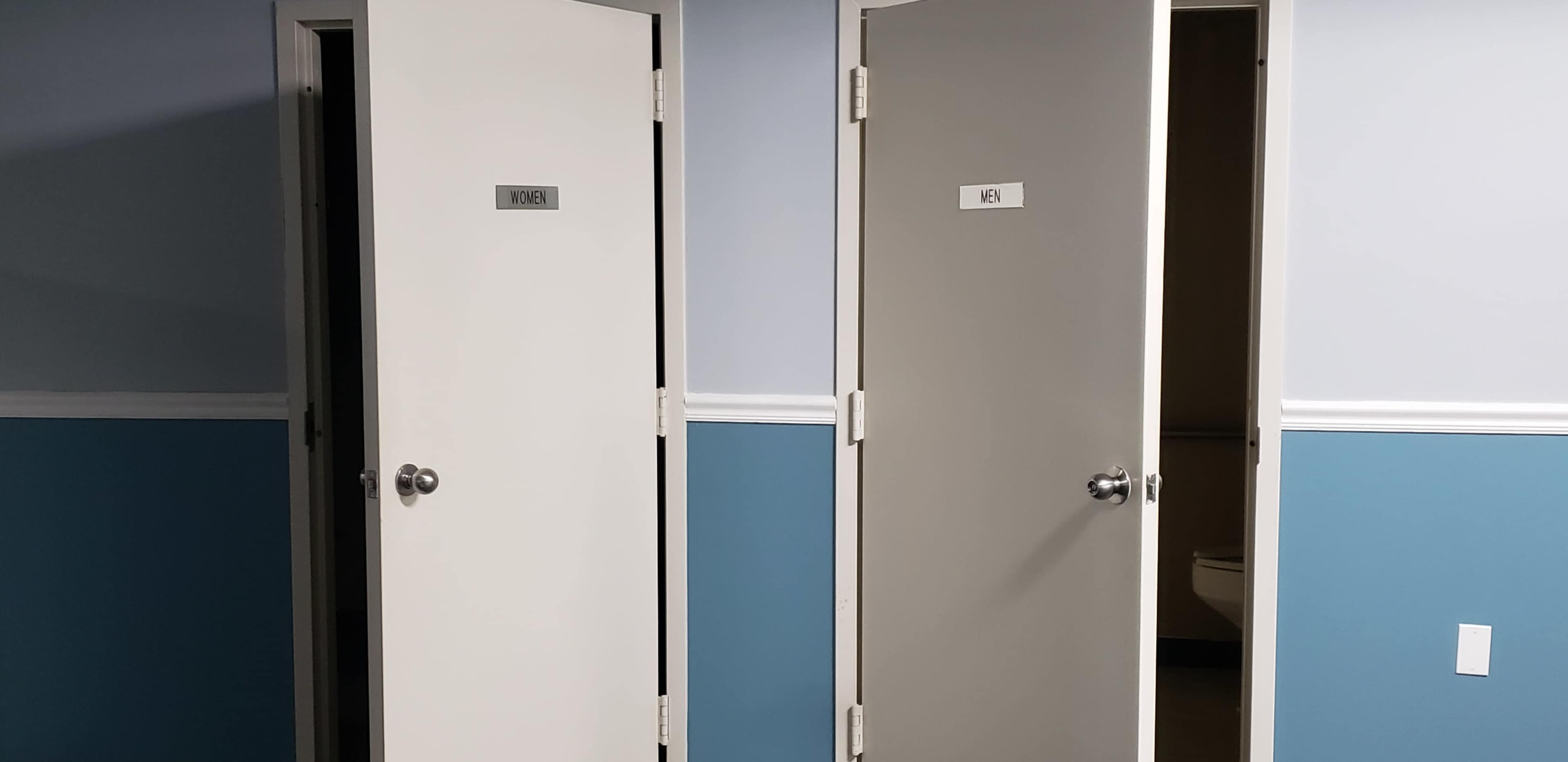 Two closed restroom doors labeled "WOMEN" and "MEN" against a blue wall.