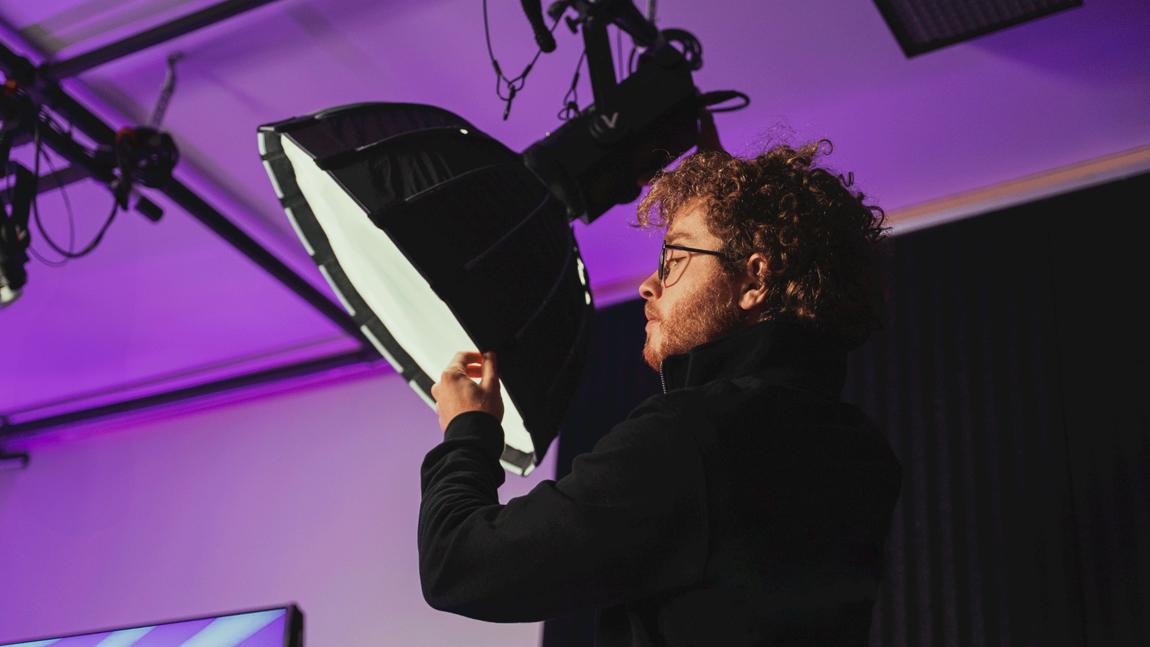 A person with curly hair adjusts a large softbox light in a studio setting.