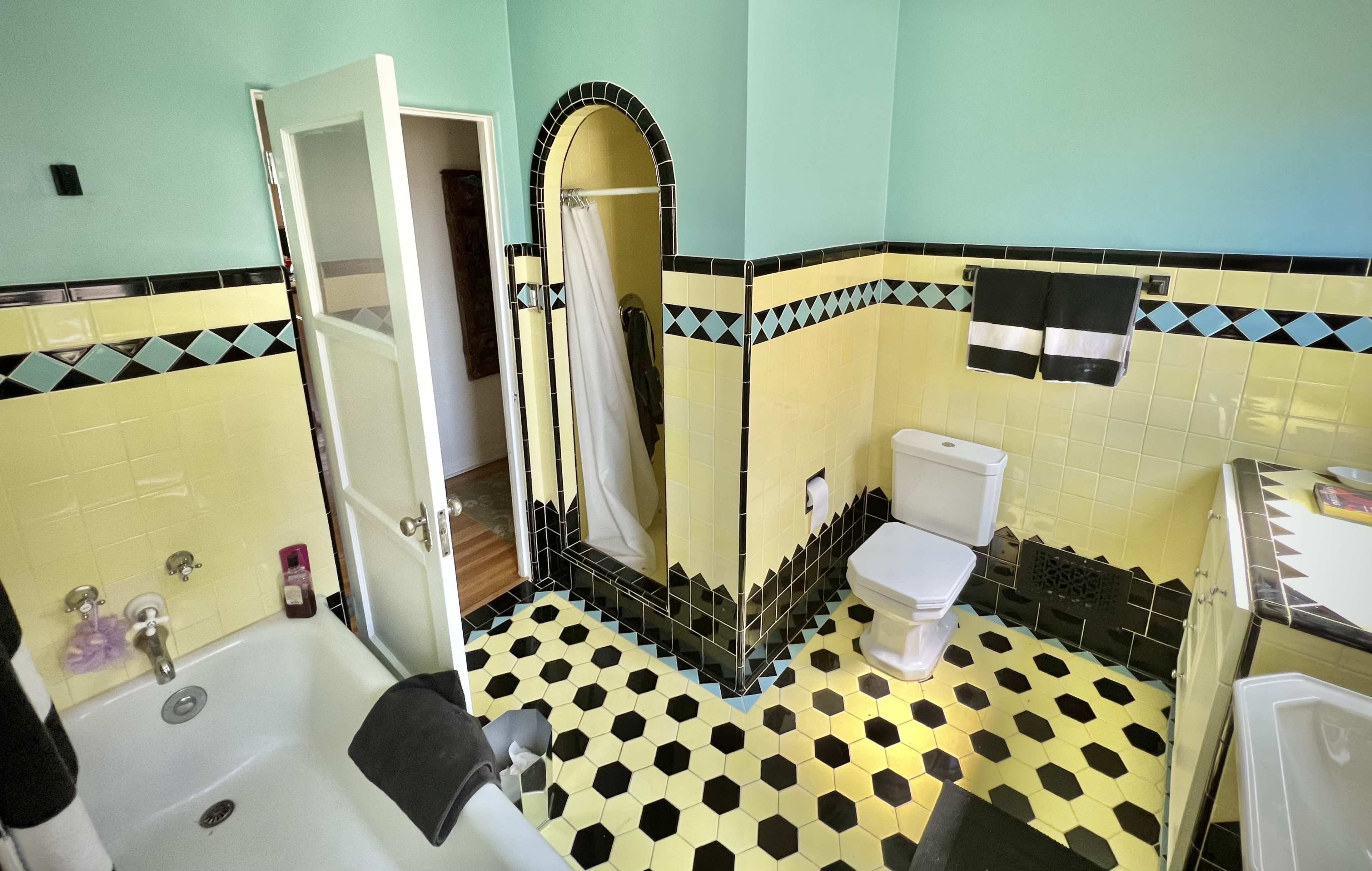The bathroom features a bathtub, a toilet, and a walk-in shower, with a color scheme of yellow and black tiles.