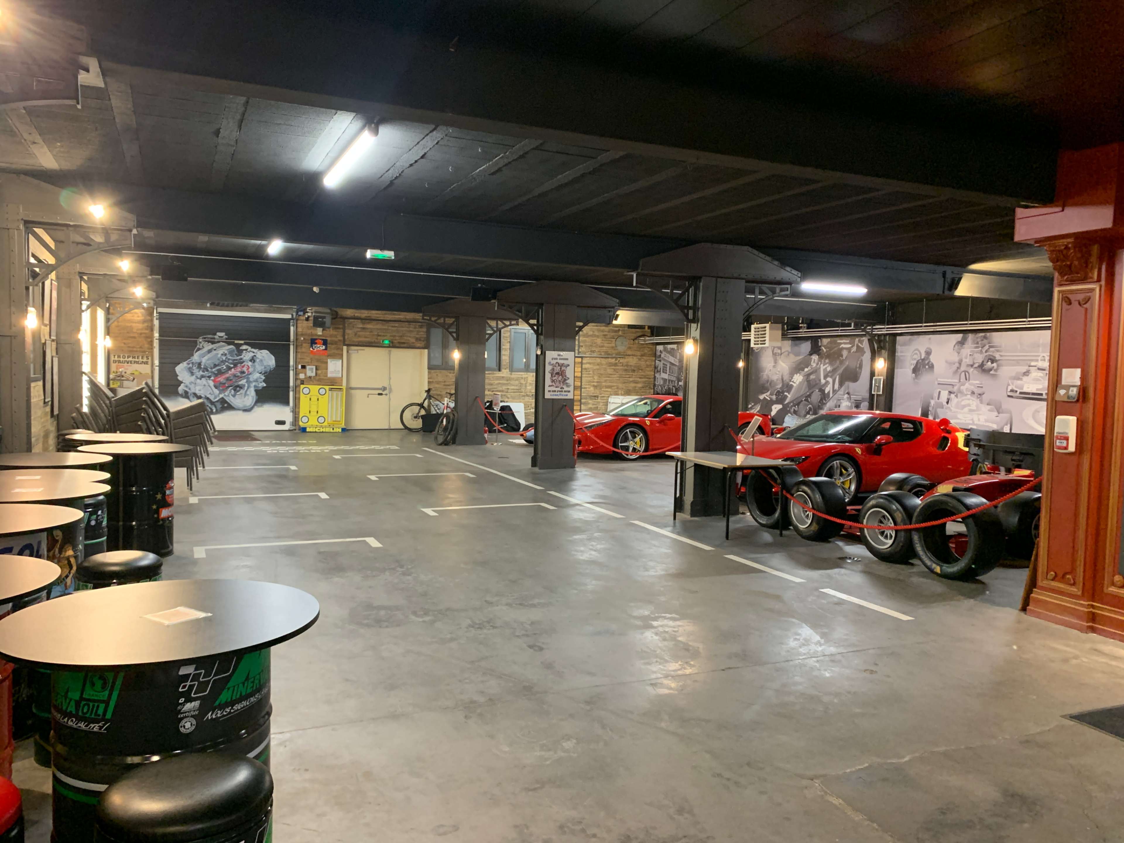 The image shows a spacious garage with several parked cars, including two red sports cars, under dim lighting and industrial-style decor.