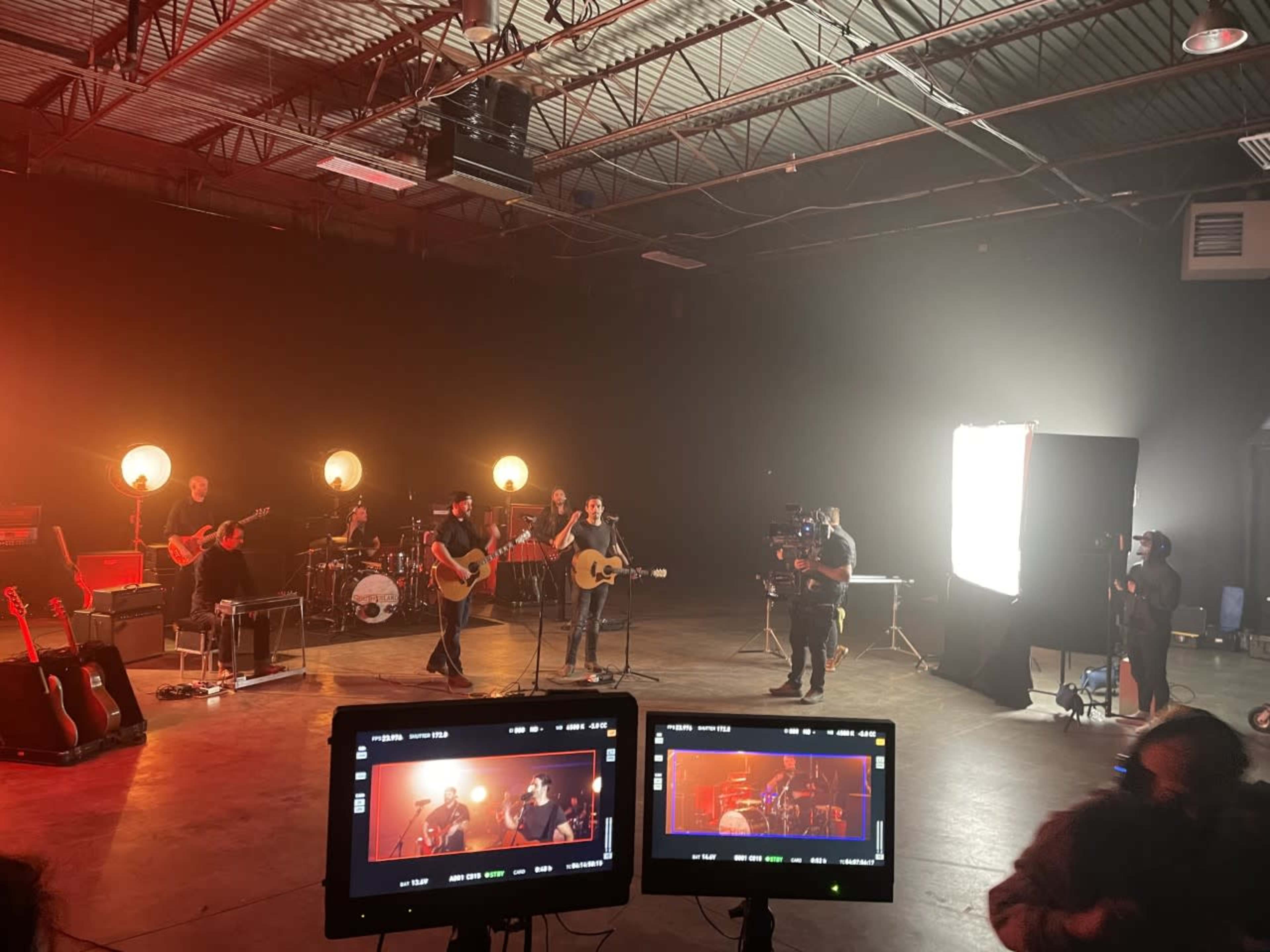 A band performs on stage in a dimly lit studio surrounded by cameras and bright lights.