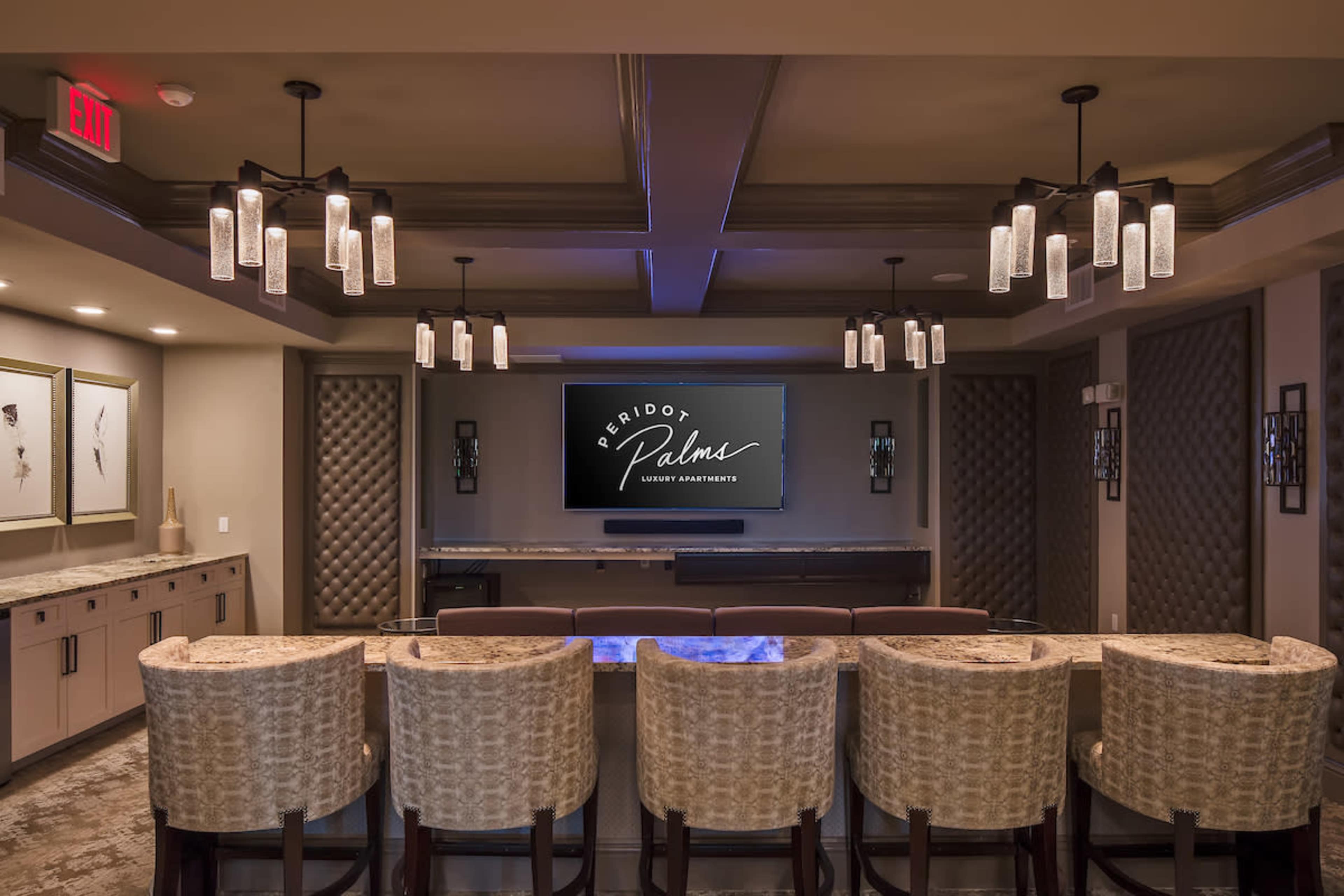 A modern lounge area with dim lighting, featuring a large screen and multiple bar stools arranged in front of it.