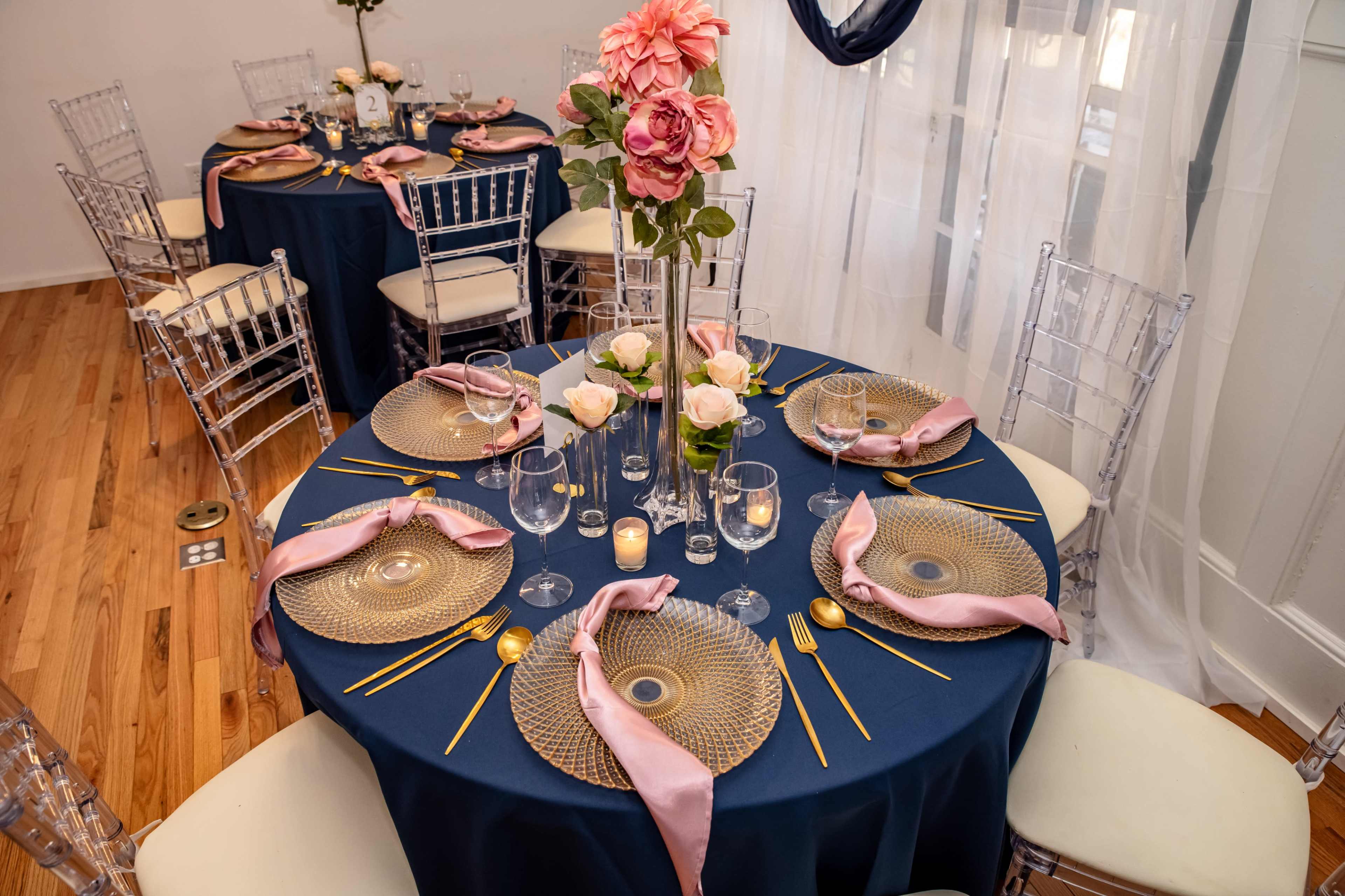 Elegantly arranged dining tables with navy tablecloths, charger plates, and floral centerpieces.