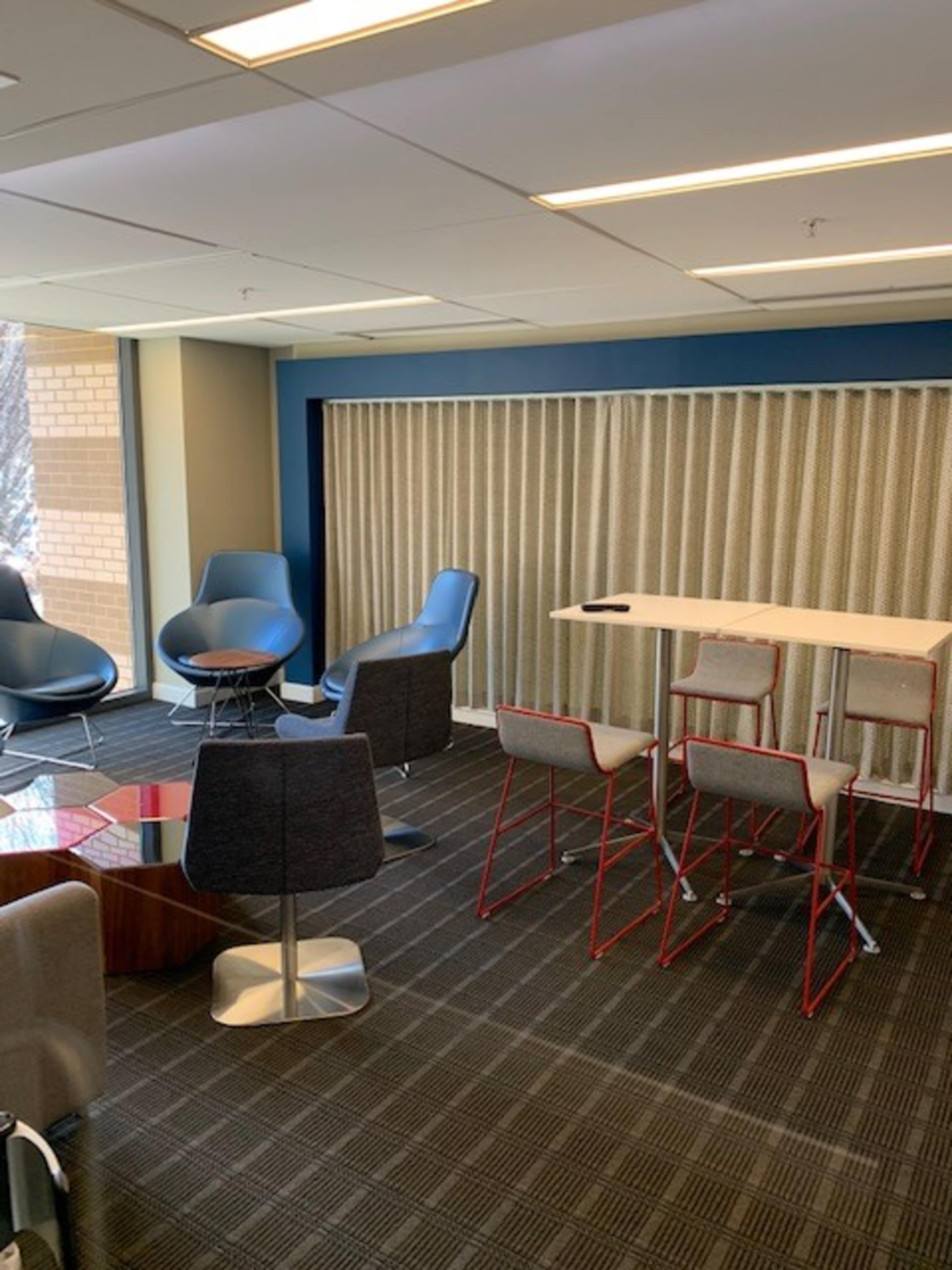 A modern office lounge area with various seating options, including chairs and barstools, and a communal table.