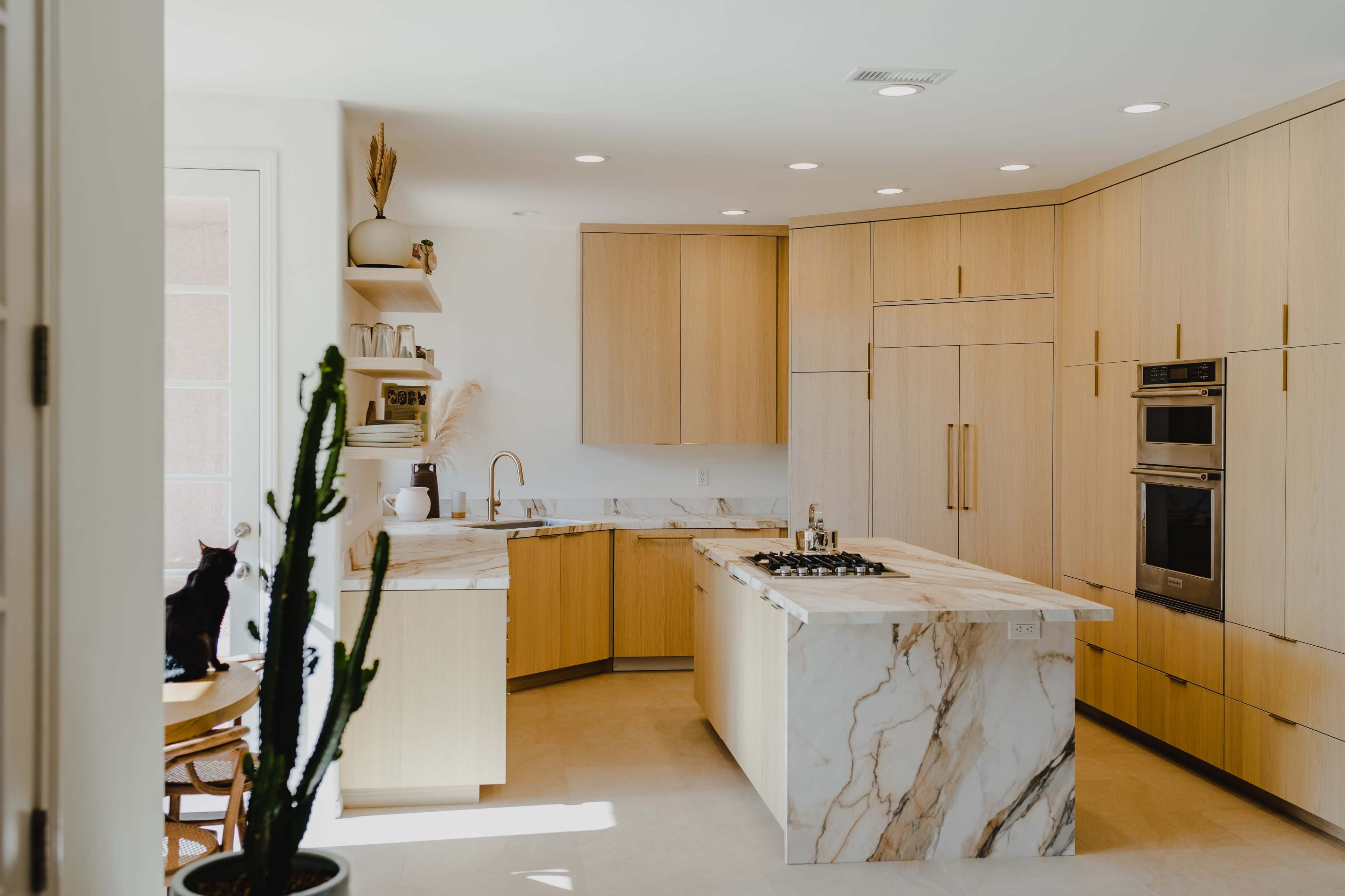 The image features a modern kitchen with light wood cabinetry, a marble countertop island, and a minimalist design.