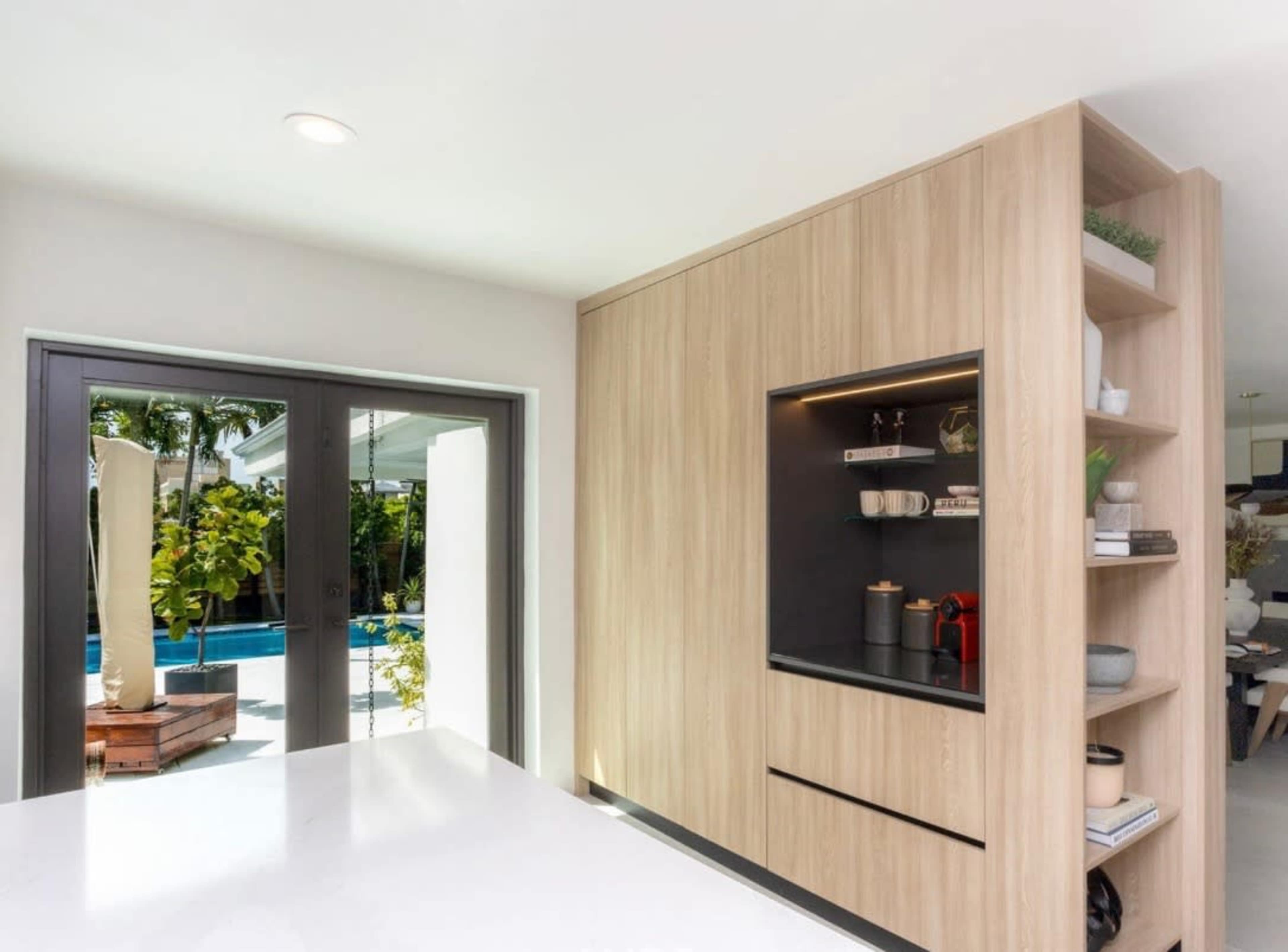 A modern kitchen with wooden cabinetry and a view of a pool area through large glass doors.
