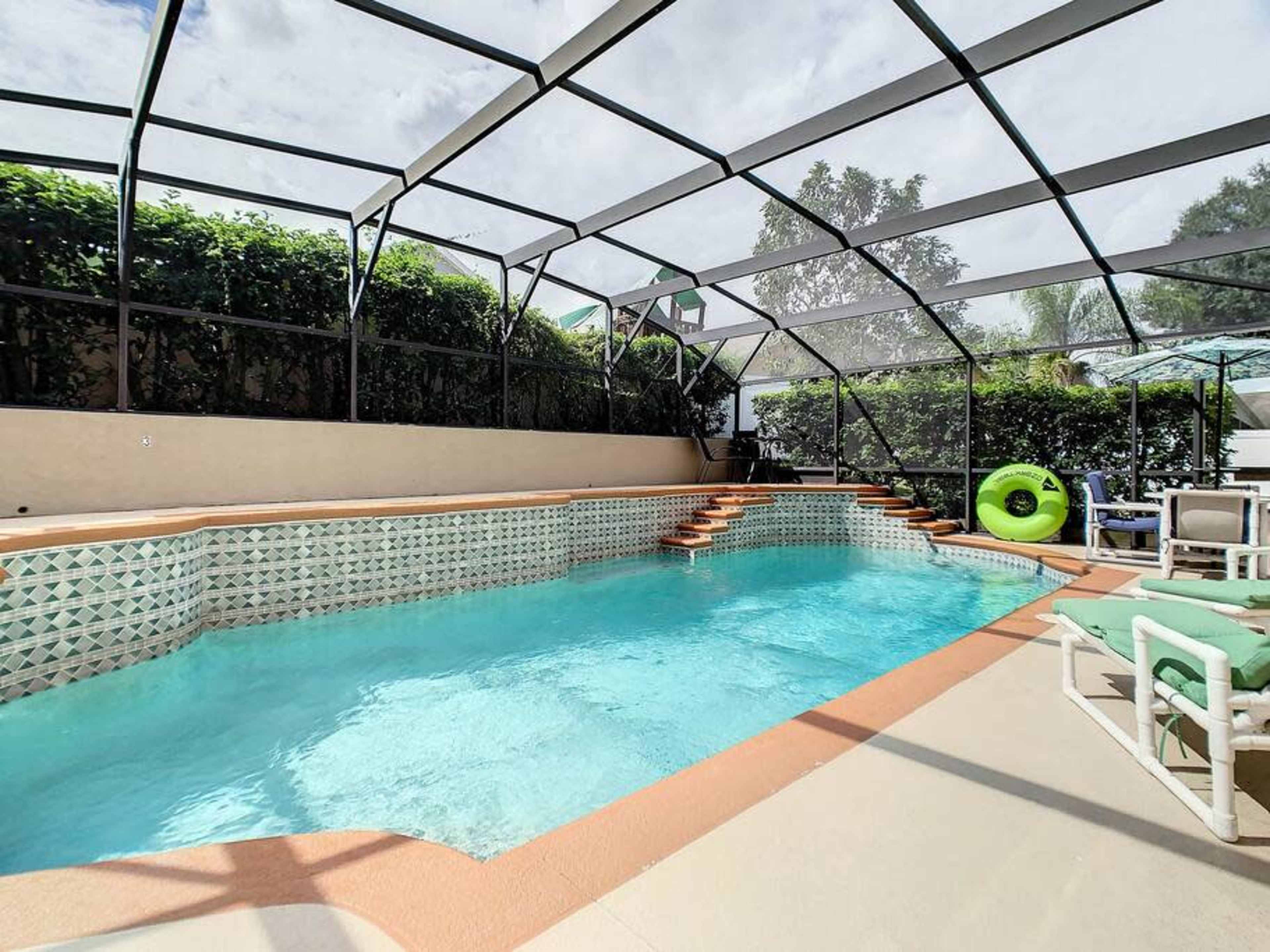 The image shows a rectangular swimming pool enclosed by a screened patio, featuring blue water and a light-colored deck.