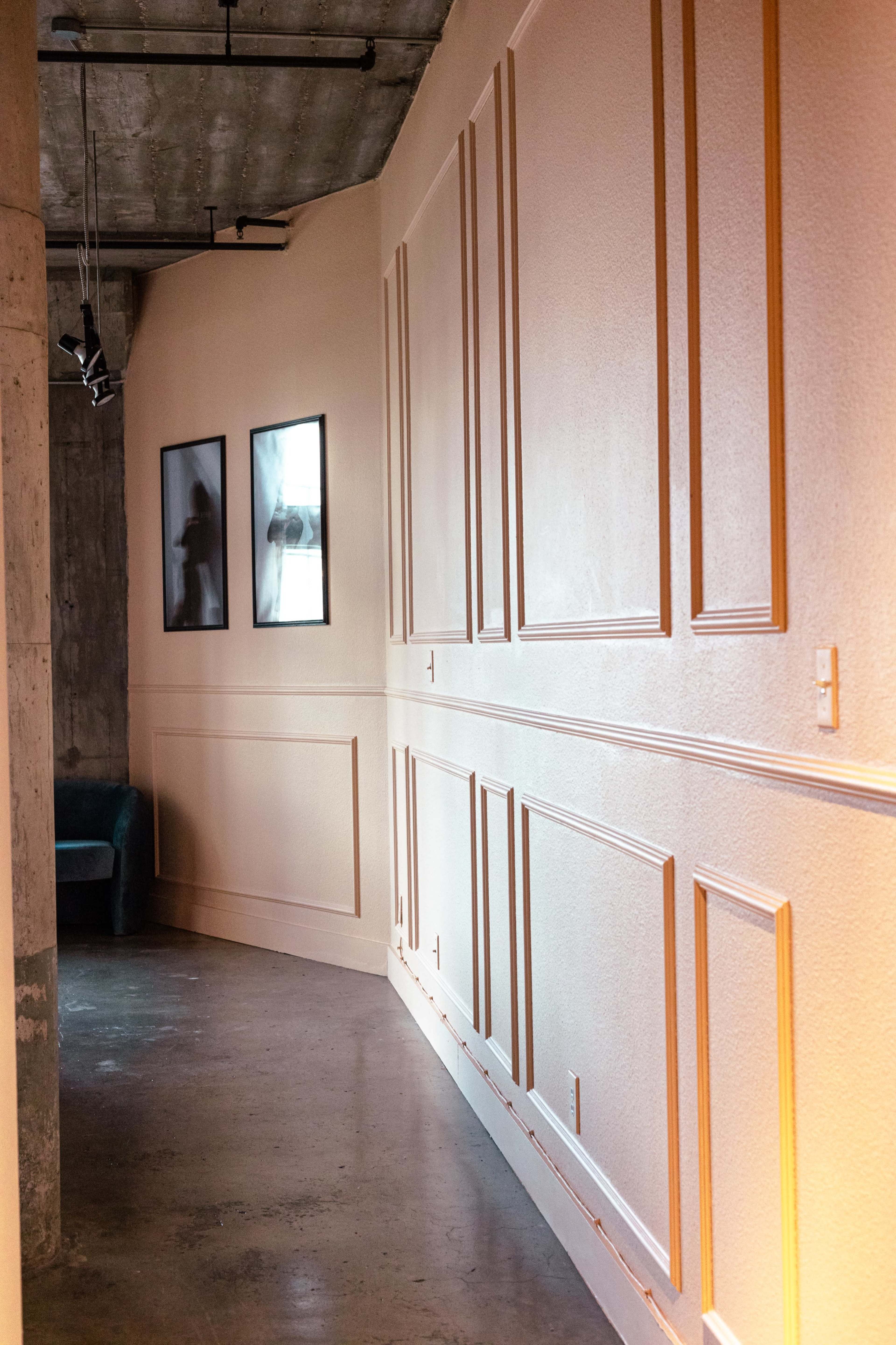 A curved hallway features framed photographs on one wall and a green sofa on the opposite side.
