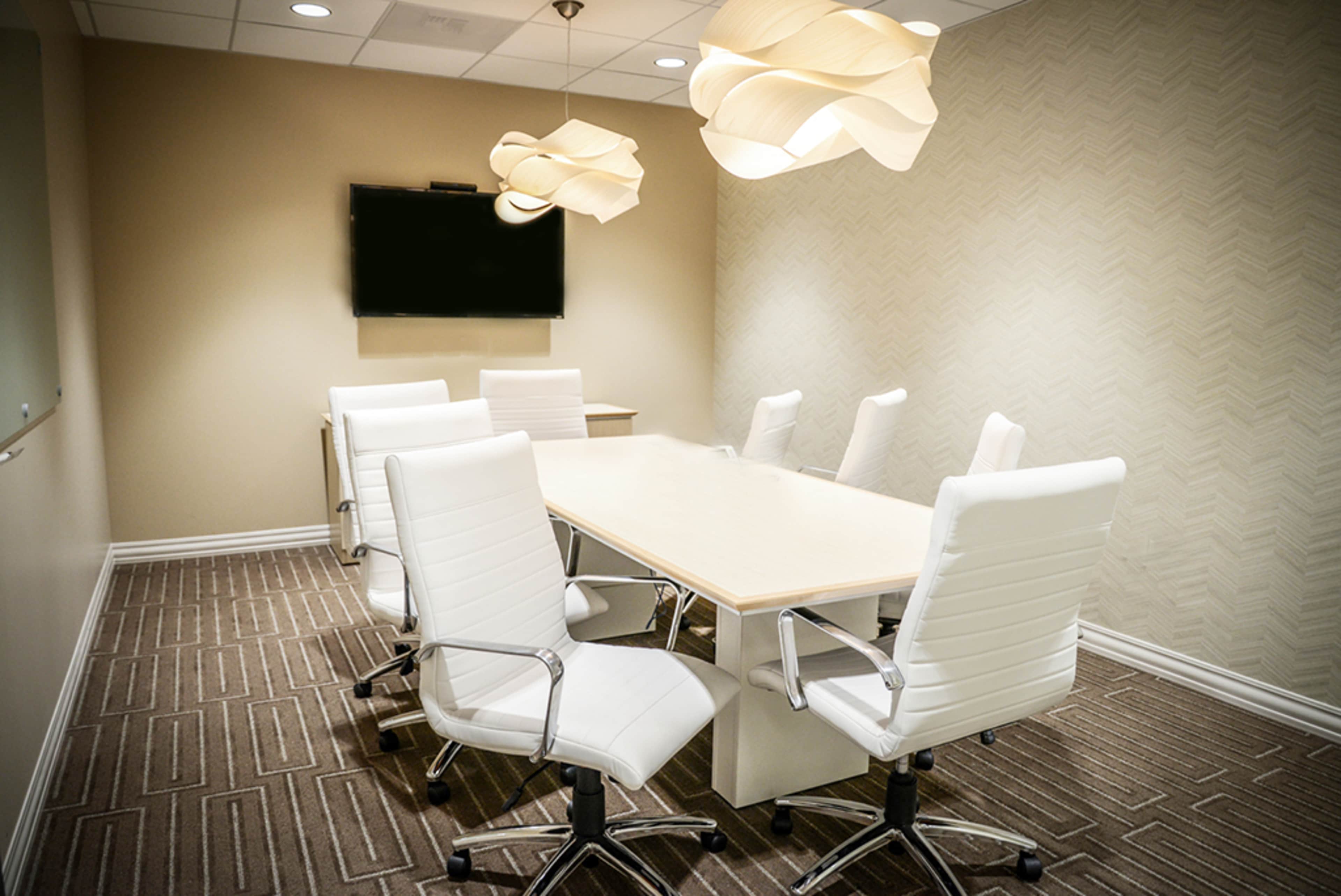 A modern conference room with a large table surrounded by six white ergonomic chairs and two pendant lights hanging from the ceiling.