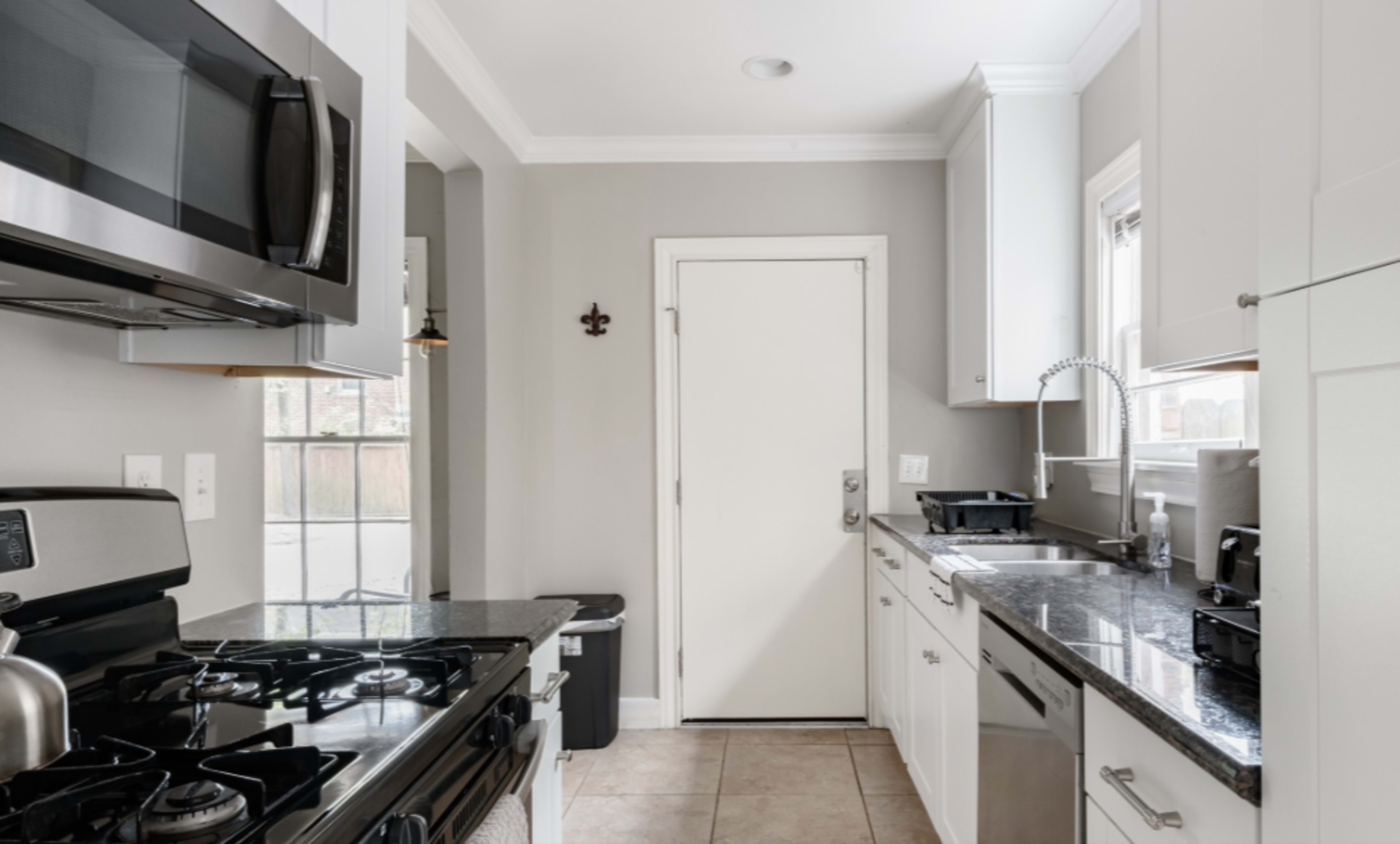 A small kitchen features stainless steel appliances, granite countertops, and a door leading outside.