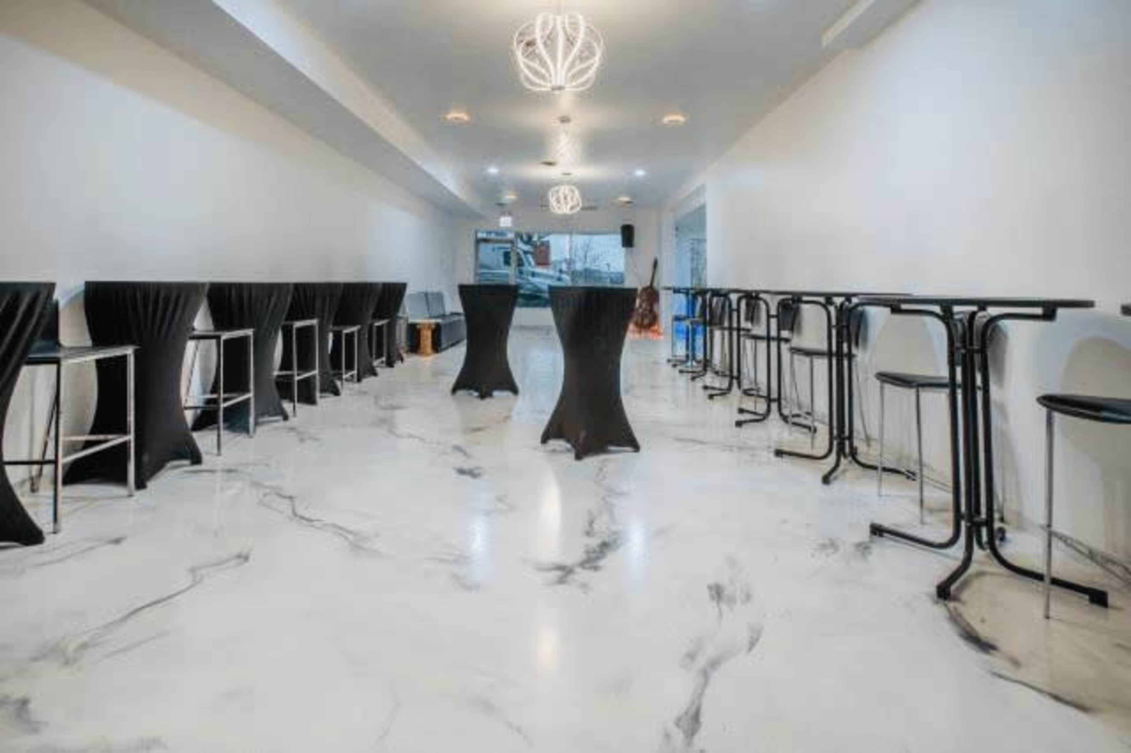 The image shows a modern, minimalist interior with black high tables and chairs set against a white marble floor.