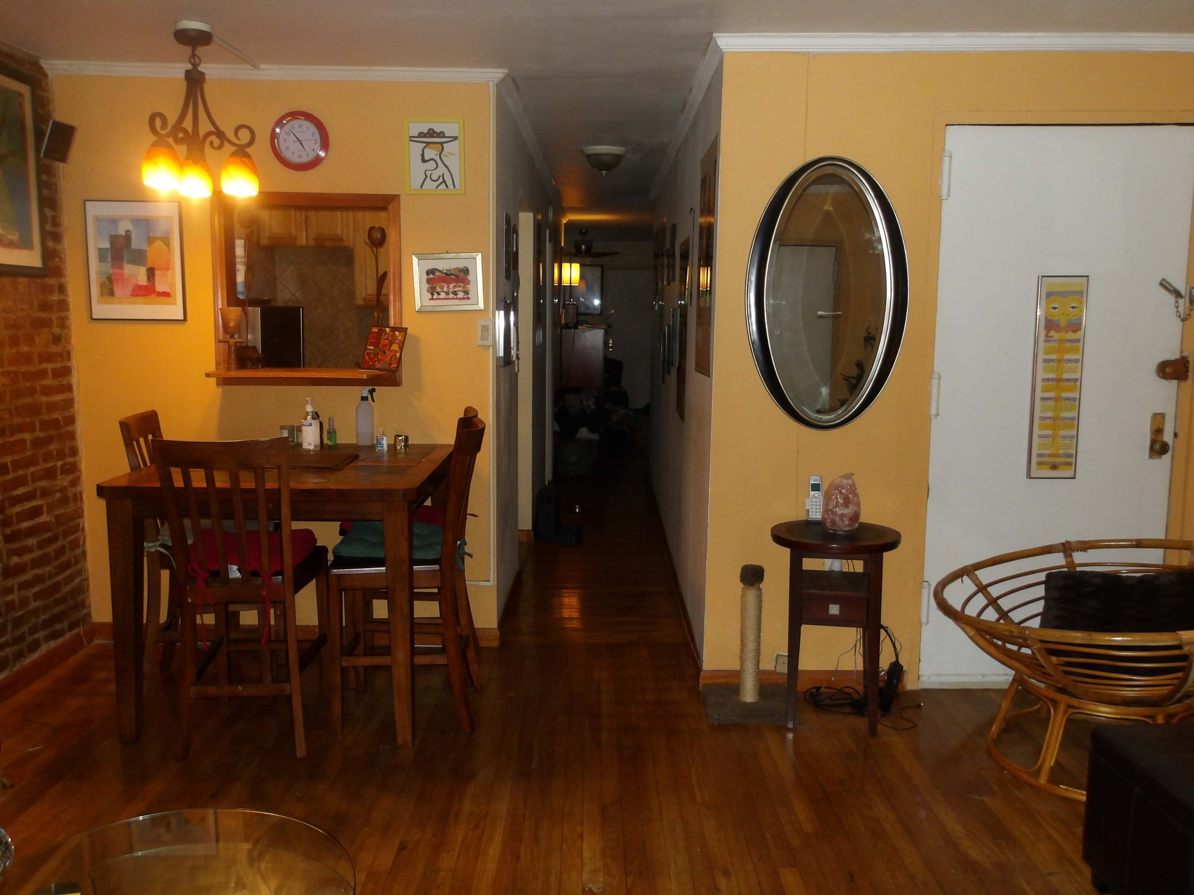 A cozy interior space featuring a dining area with a small table and chairs, a hallway leading to a door, and a circular mirror on the wall.