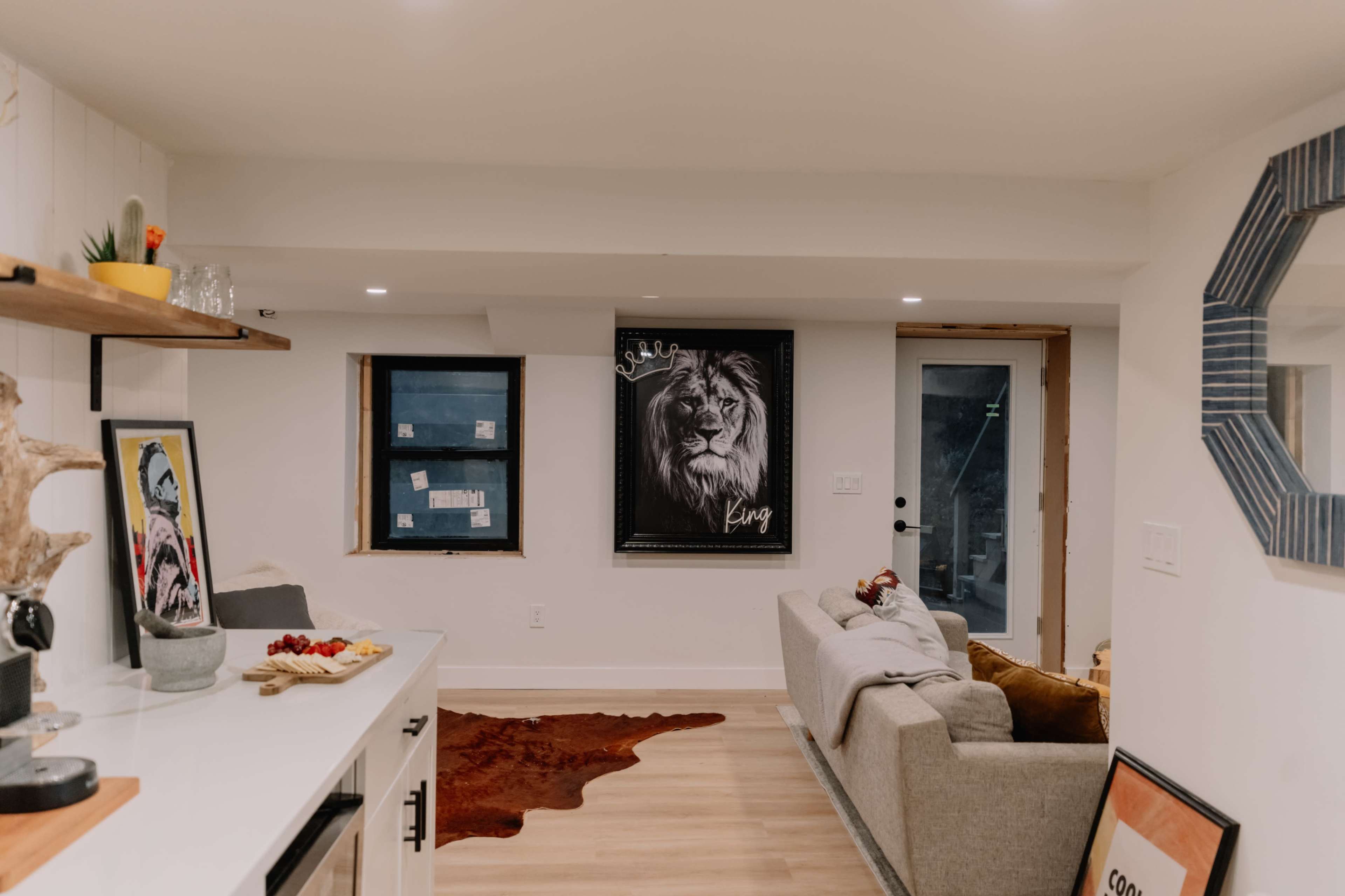 The image shows a cozy living area with a gray sofa, a wall featuring a lion poster, and a small window beside it.