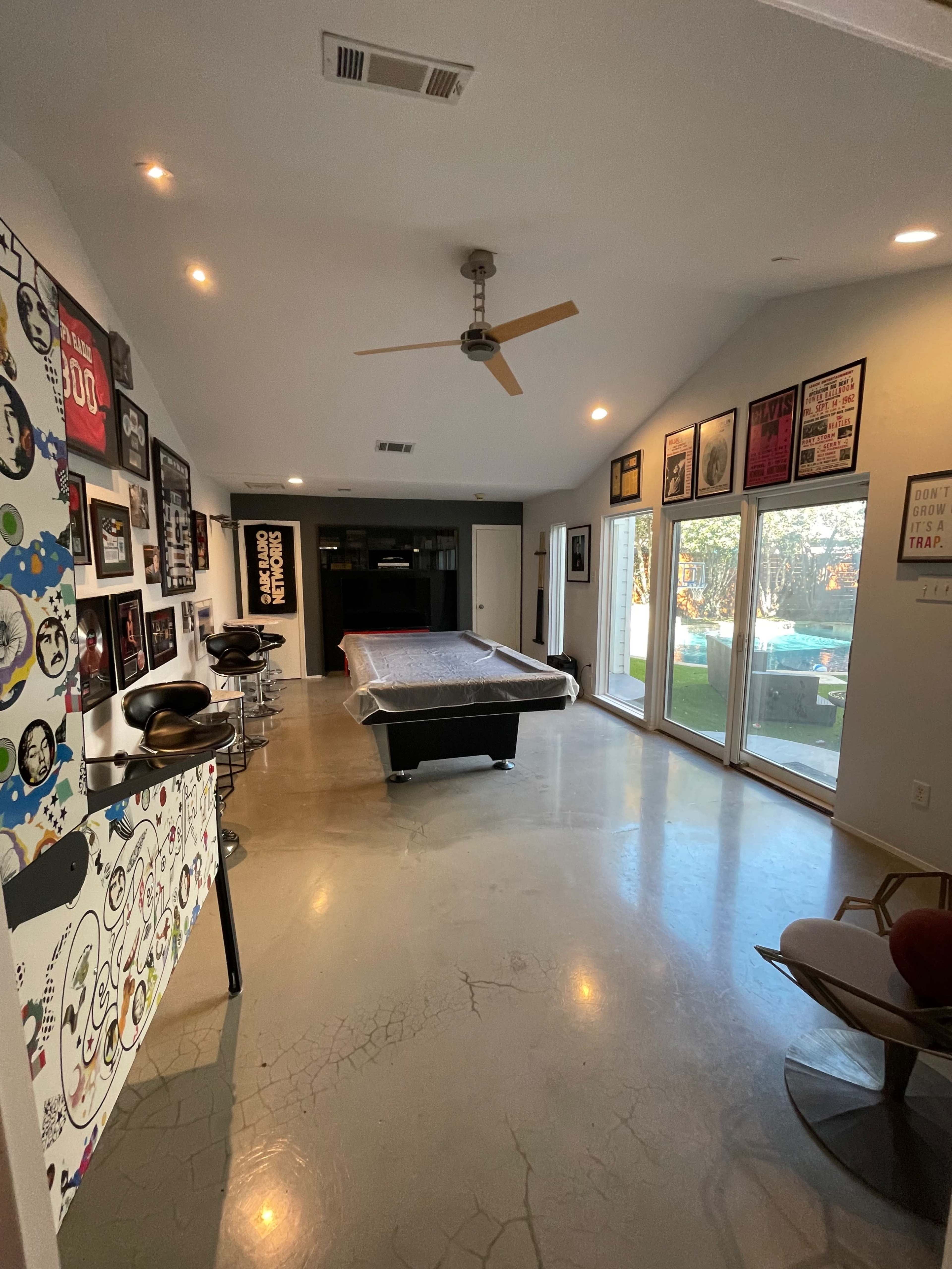 A spacious game room featuring a pool table, modern seating, and walls adorned with various framed posters.