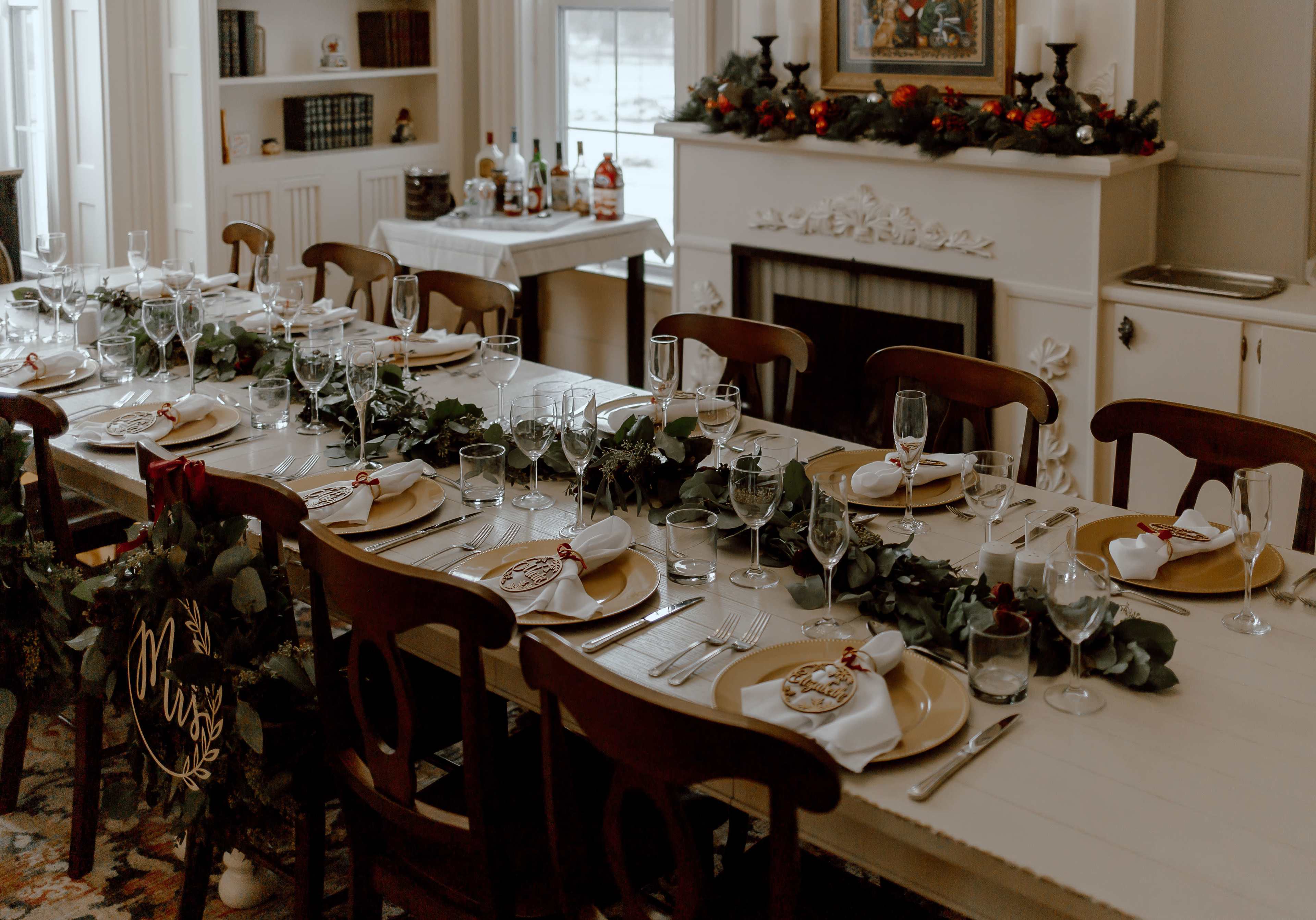 A long dining table is set with plates, glasses, and decorative greenery, ready for a formal meal in an elegantly arranged room.