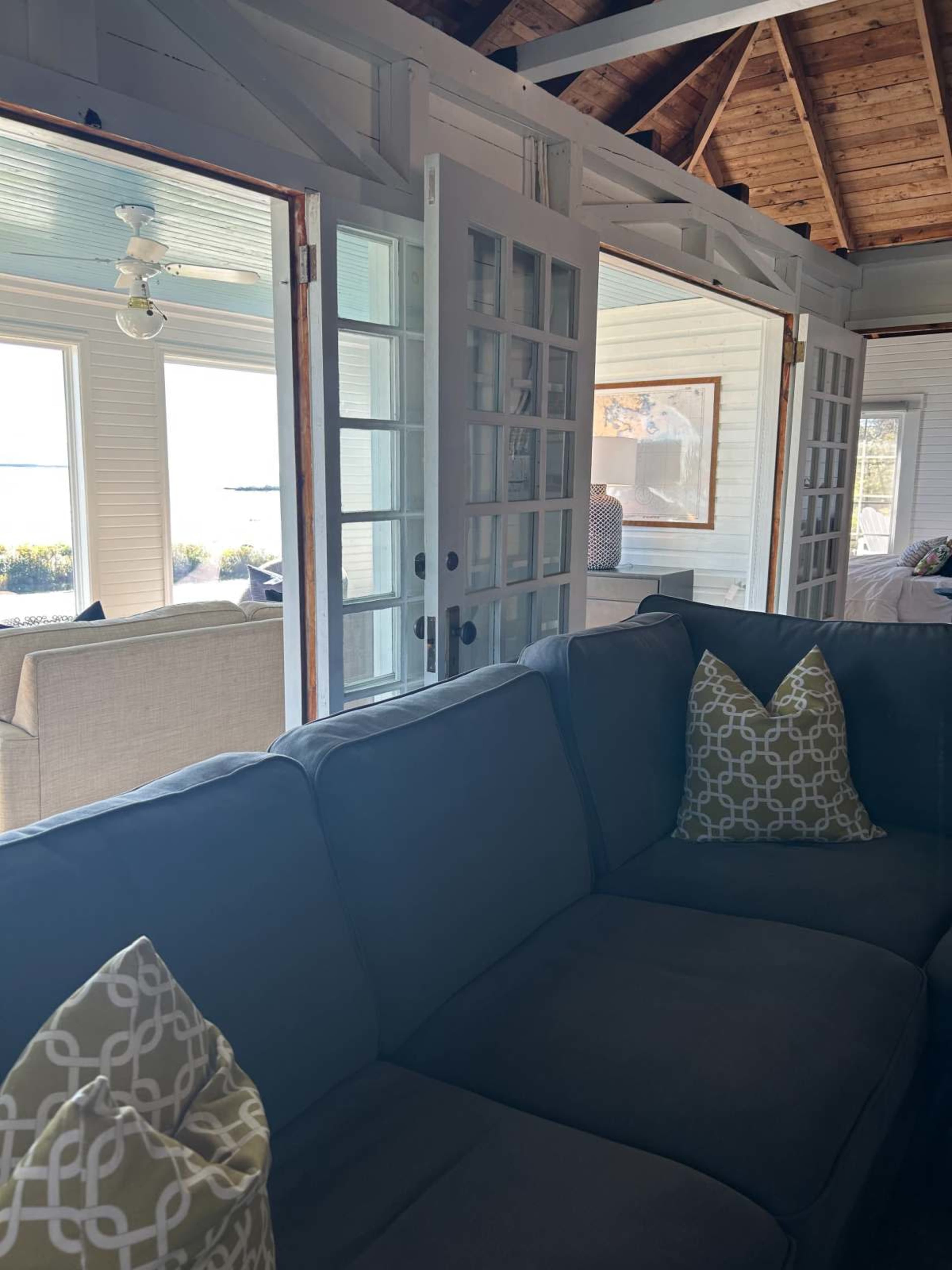 The image shows a sectional sofa with decorative pillows, positioned in a room with large glass doors that lead to a view of an outdoor area.