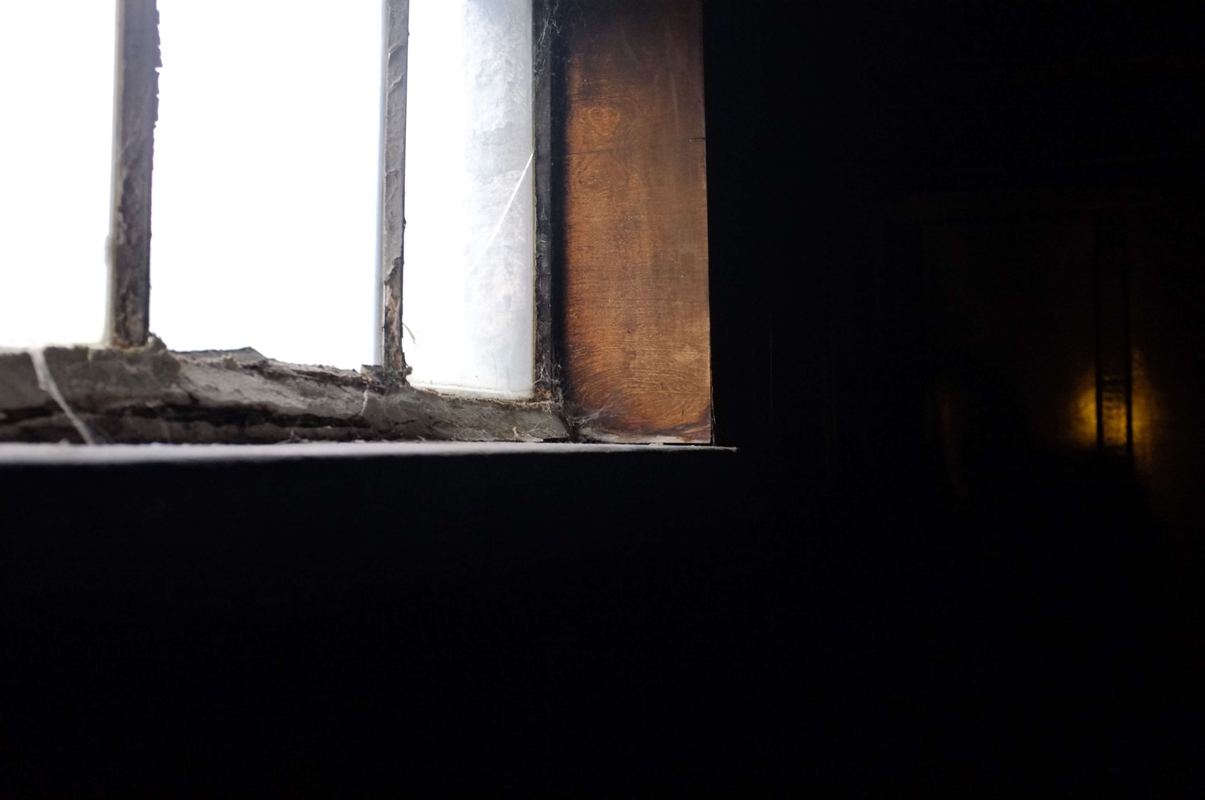 The image shows a partially illuminated window in a dark room, with visible cobwebs in the corners.