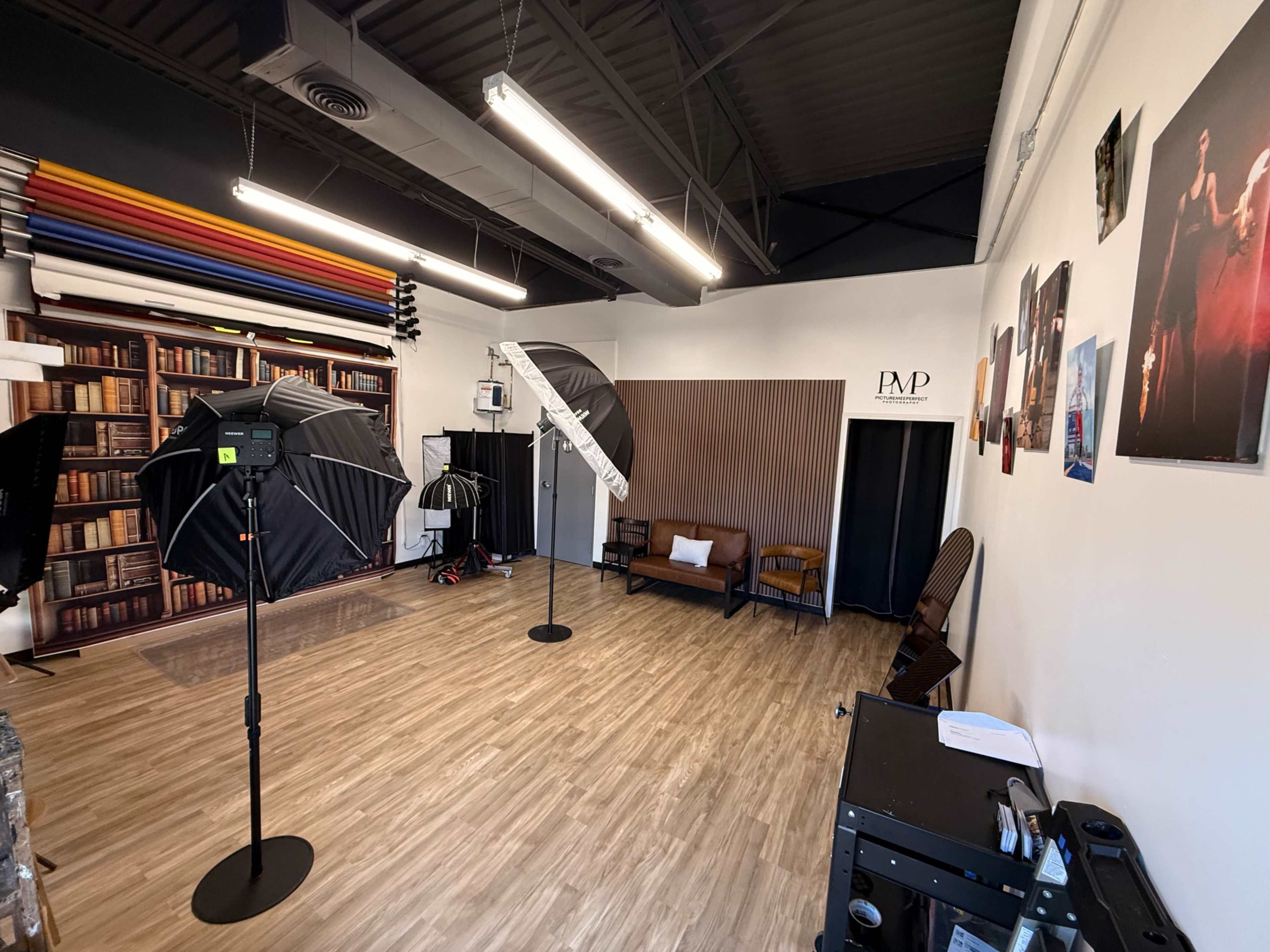 The image shows a photography studio with various backdrops, lighting equipment, and a seating area.