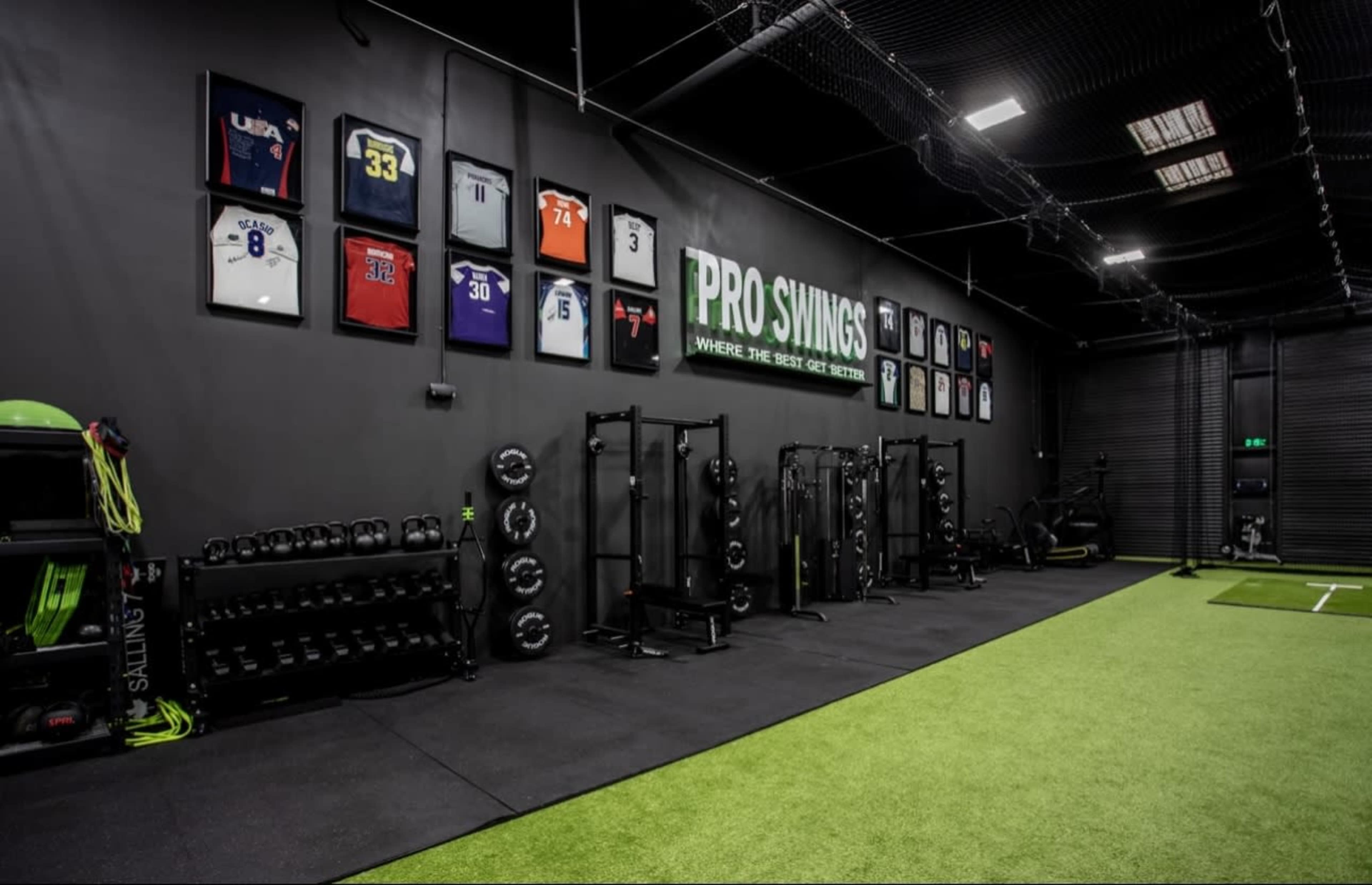 The image shows a fitness facility featuring a variety of weights, gym equipment, and framed jerseys hanging on the wall.