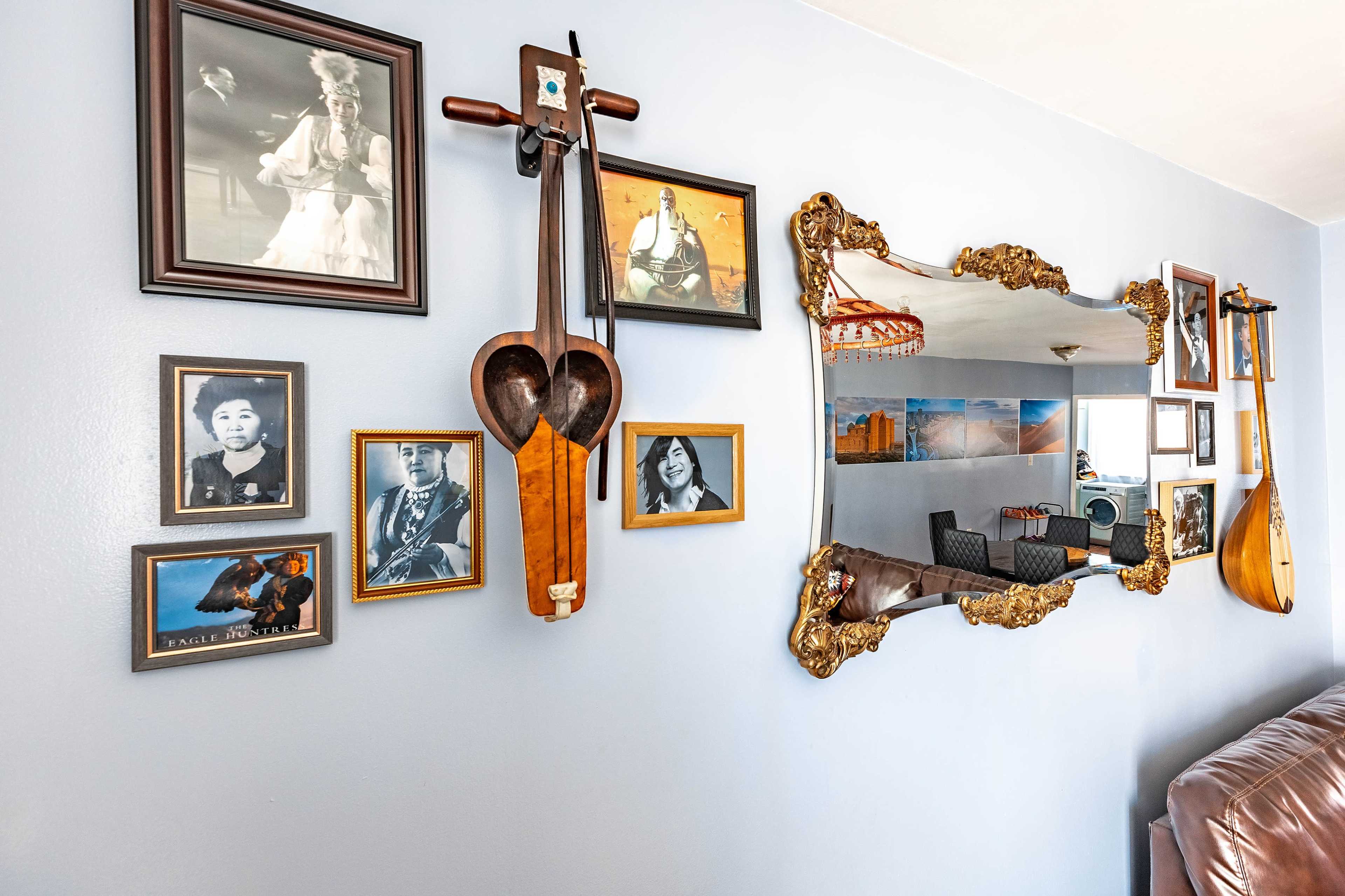 The image shows a wall adorned with framed photographs, a decorative mirror, and a wooden musical instrument.