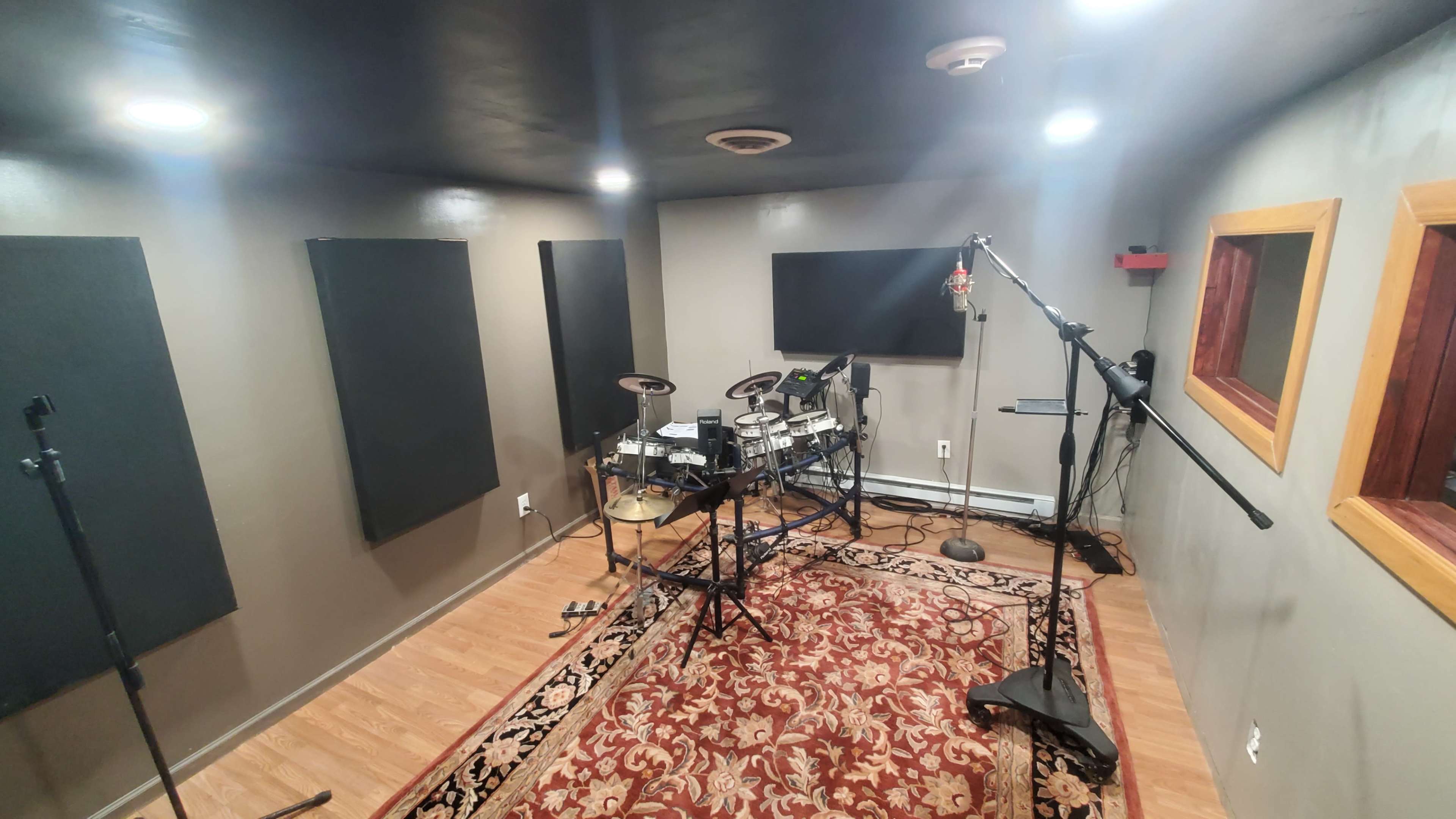 The image shows a soundproof recording studio equipped with an electronic drum set, microphones, and acoustic treatment panels on the walls.