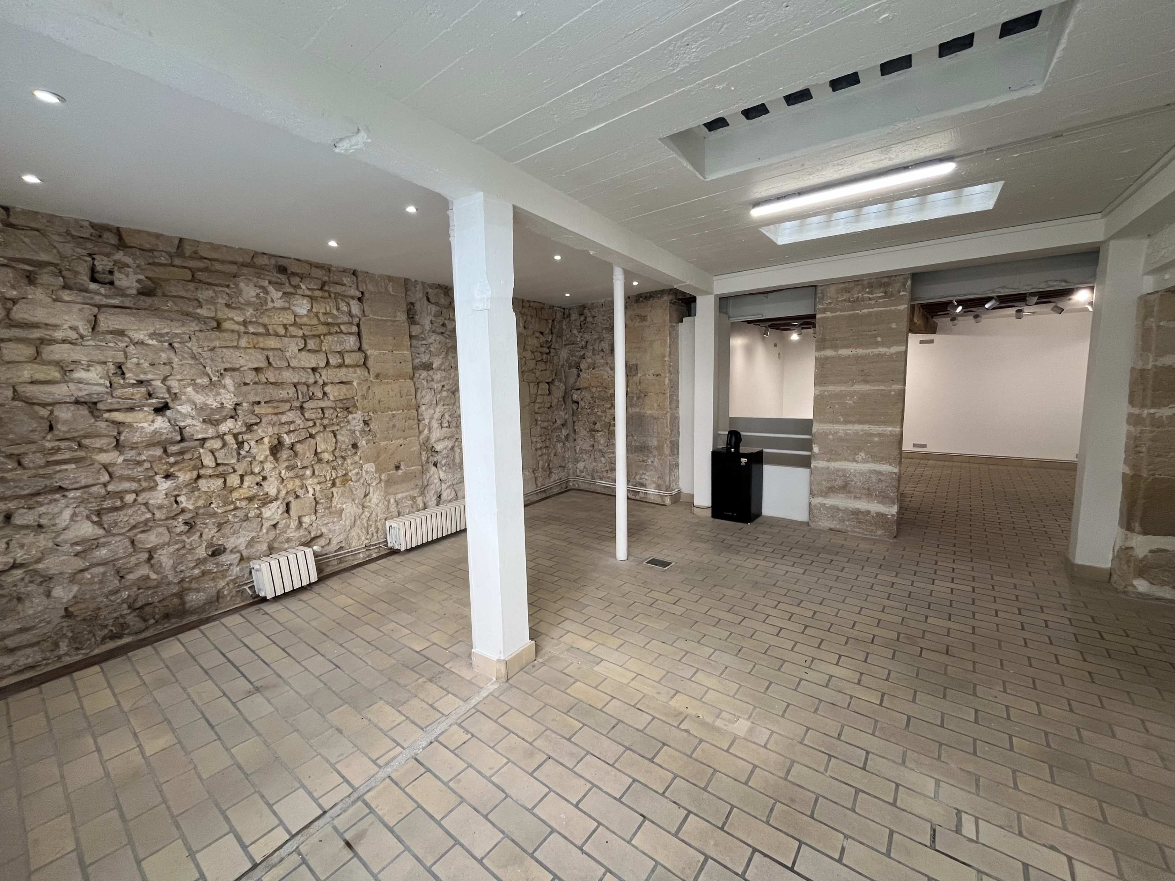 The image shows an empty room with stone walls, tiled flooring, and several overhead lights.