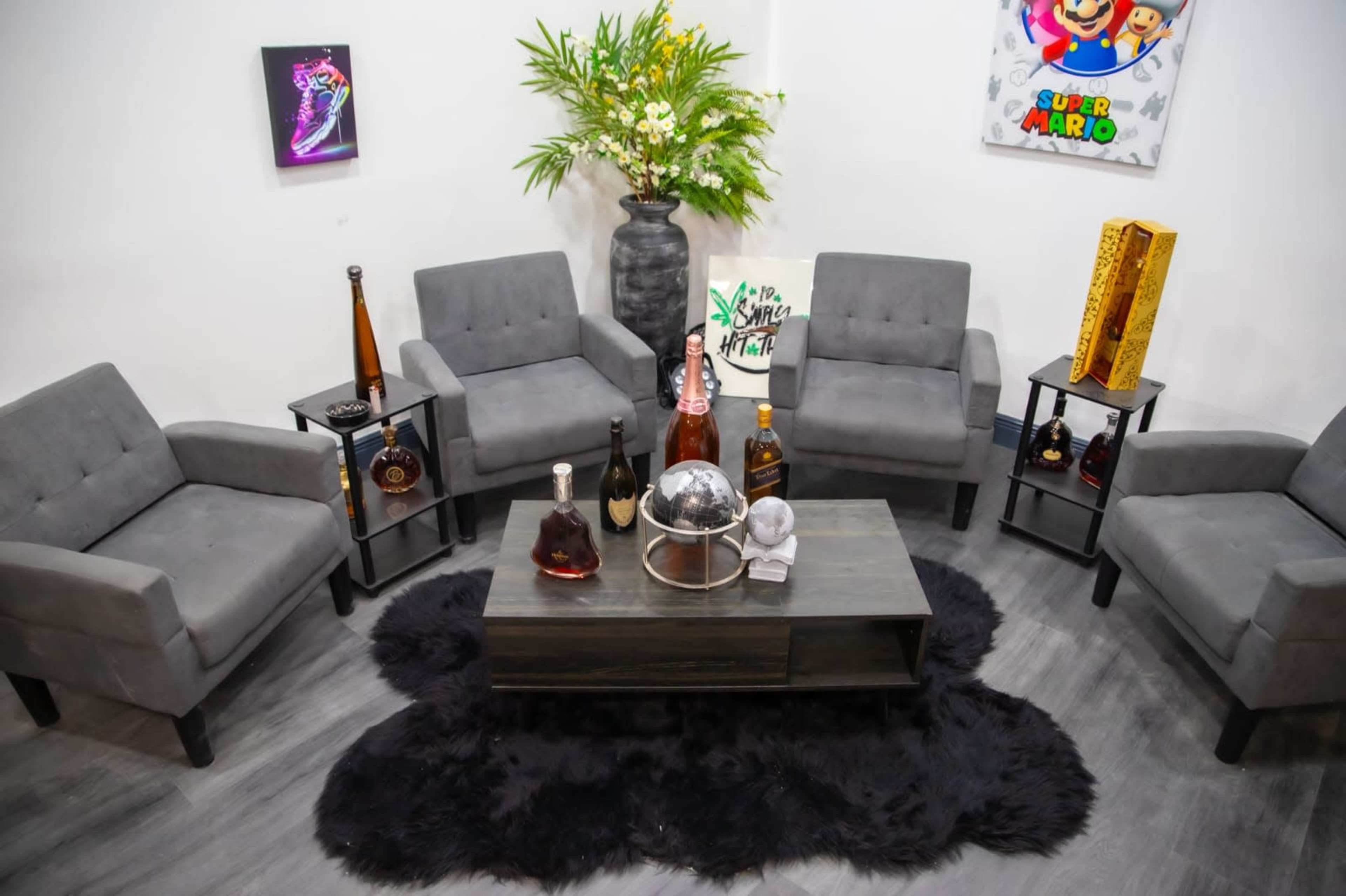 A seating area features four gray chairs arranged around a black coffee table on a black rug, with decorative bottles and a large plant nearby.