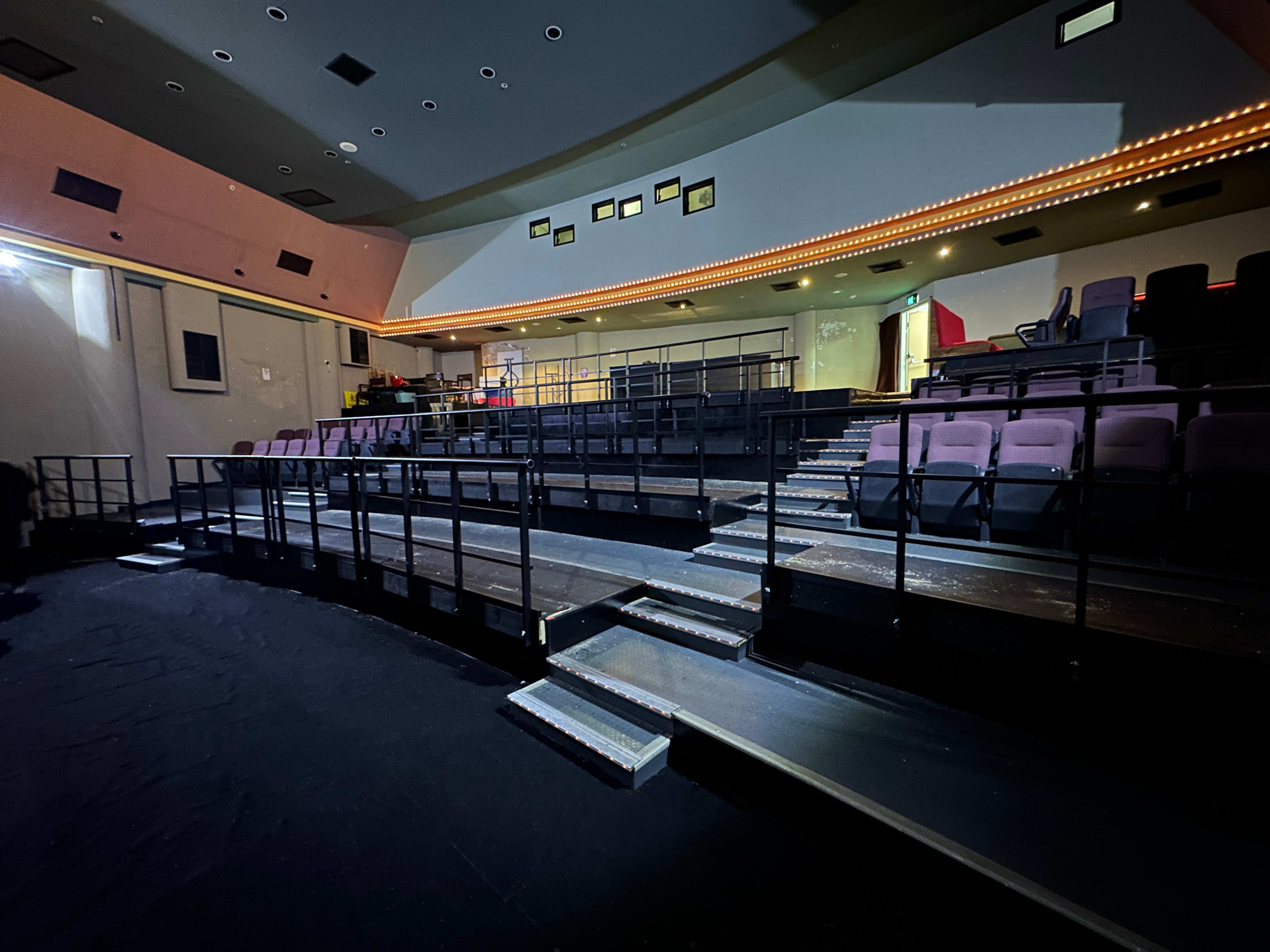 A theater interior with tiered seating, a stage area, and illuminated borders along the ceiling.