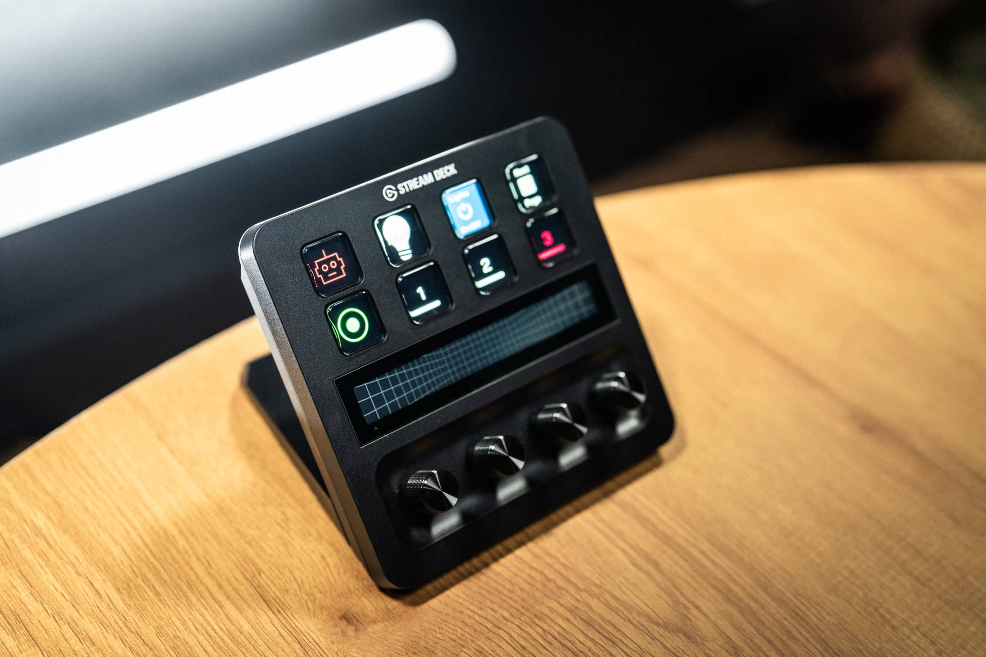 The image shows a control device with several colored buttons and dials, positioned on a wooden surface.