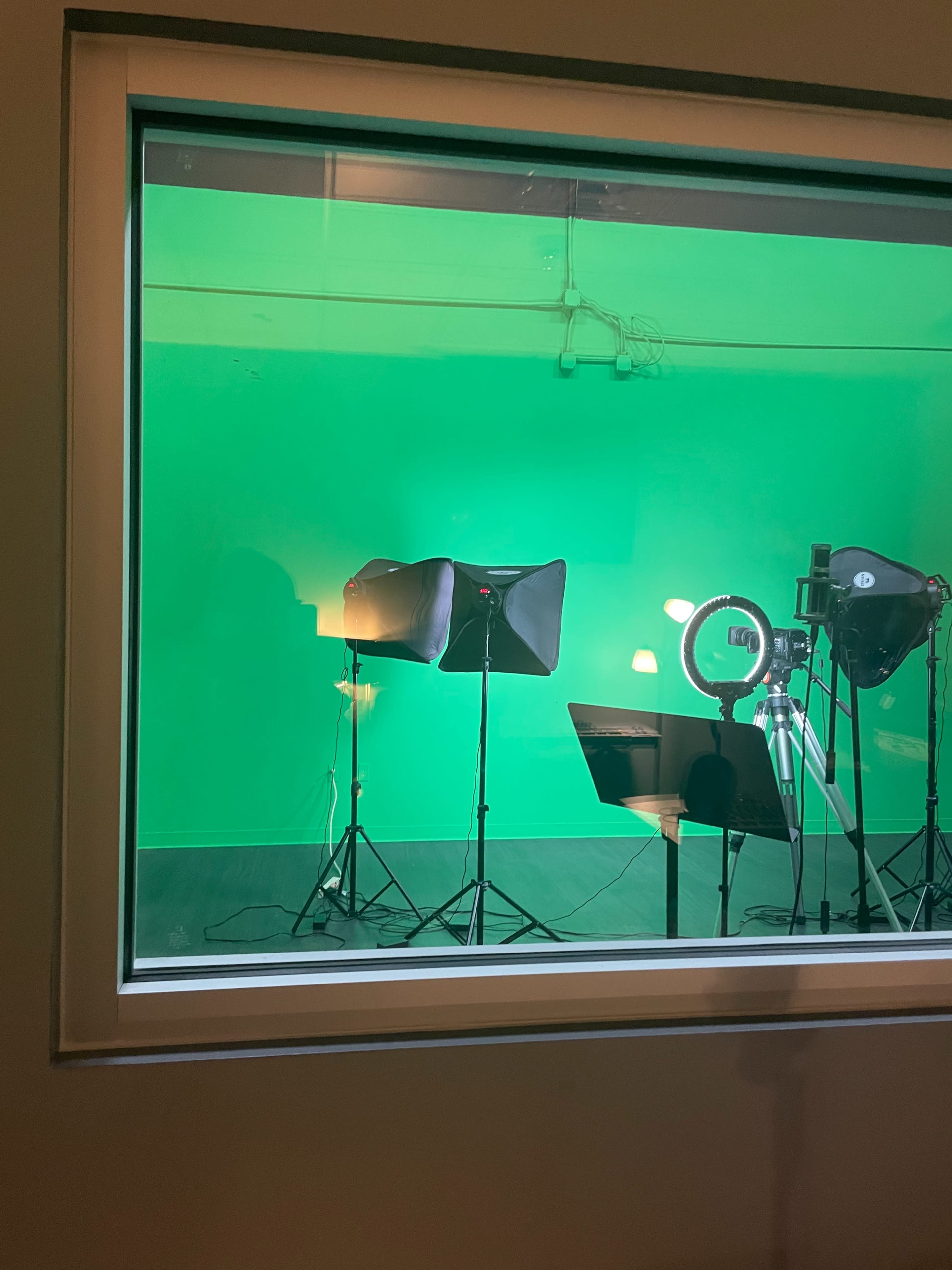 A green screen studio is set up with lighting equipment and a camera on tripods.