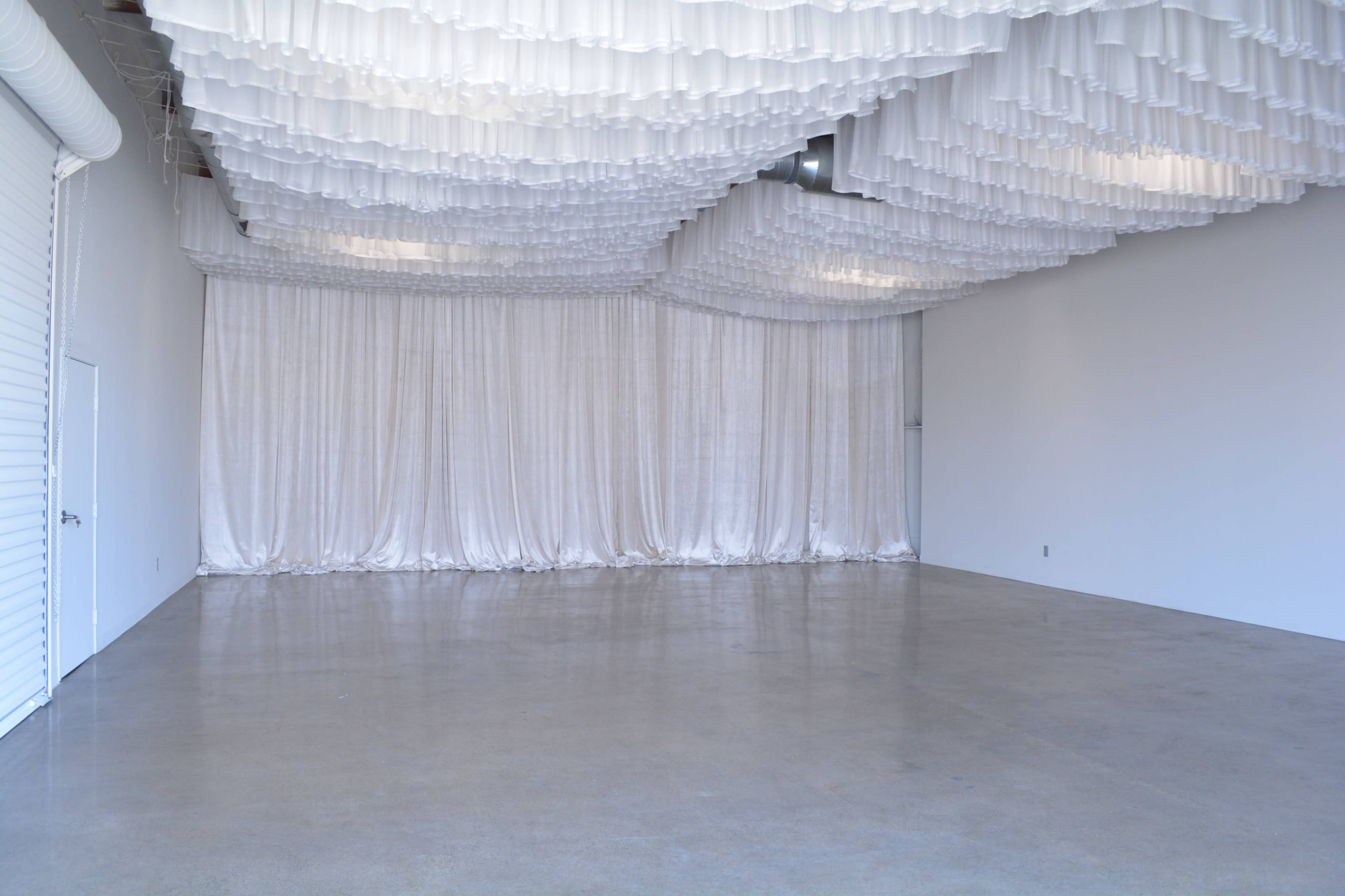 A spacious, empty room with a polished concrete floor and draped white fabric installations on the ceiling.
