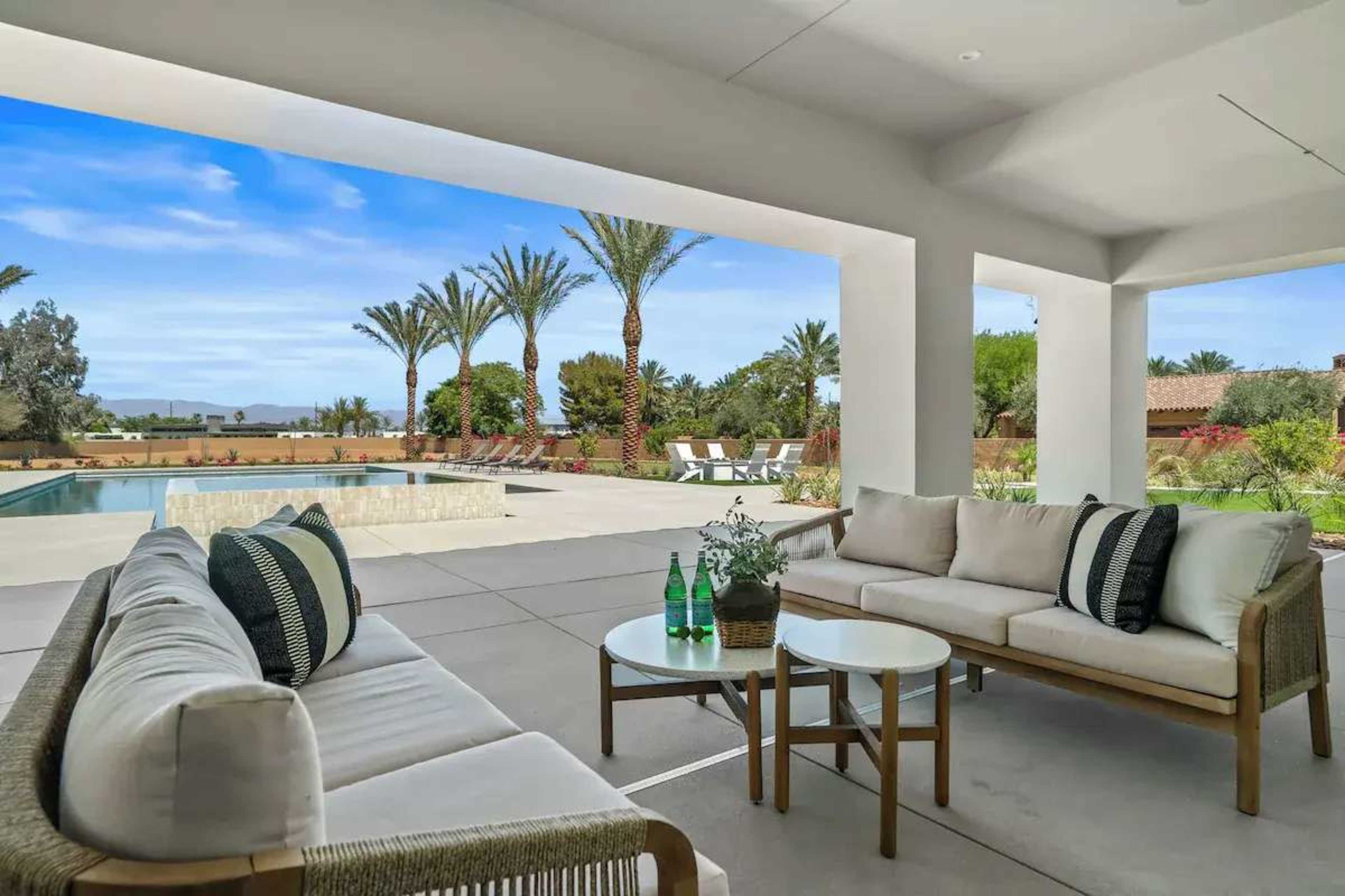 A modern outdoor living space features a comfortable seating area with a small table overlooking a swimming pool and palm trees.