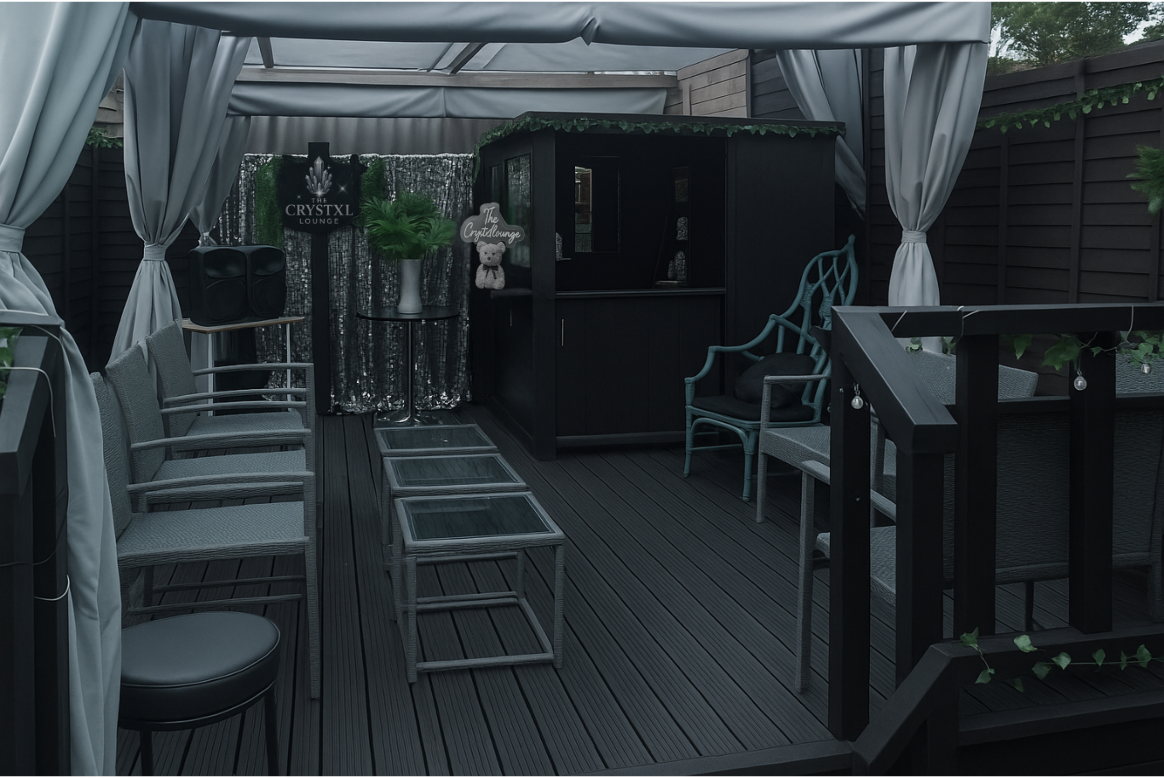 The image shows a covered outdoor seating area with dark wooden flooring, several chairs, a table, and a small bar area adorned with decorative elements.