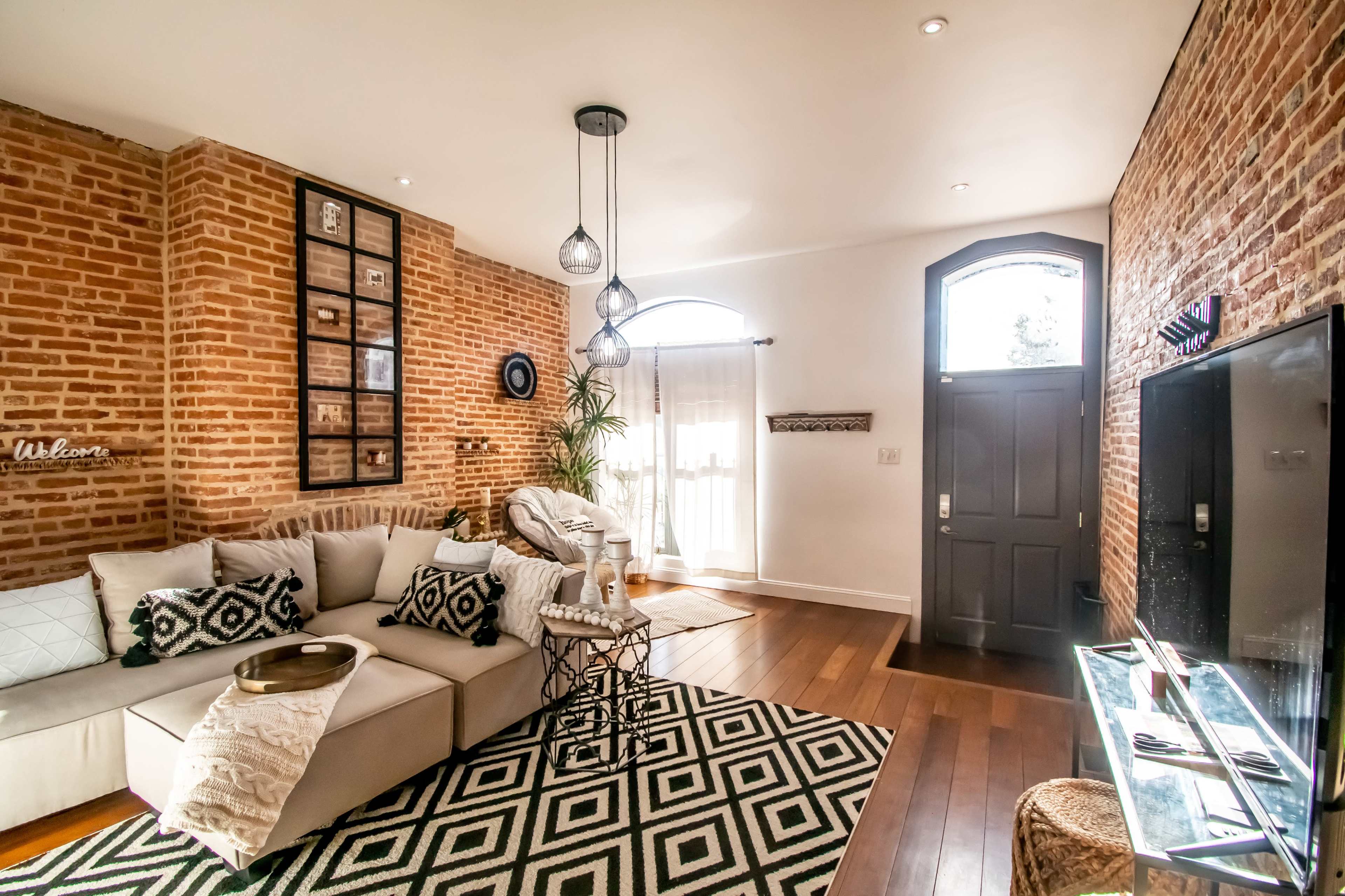 A modern living room with a brick wall, a sectional sofa, and a geometric patterned rug.