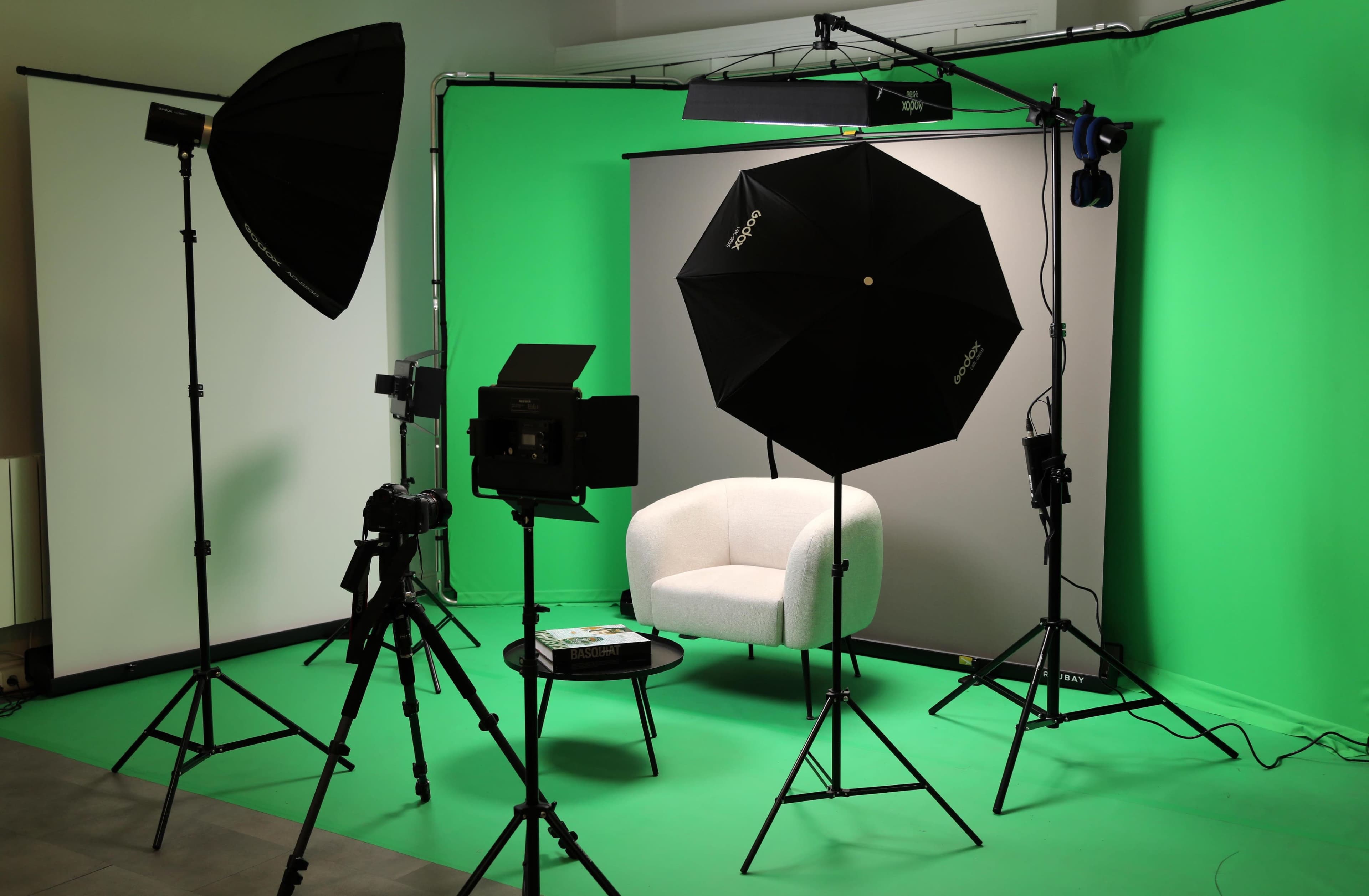 The image shows a photography setup with a white chair, a table, and multiple light sources in front of a green backdrop.