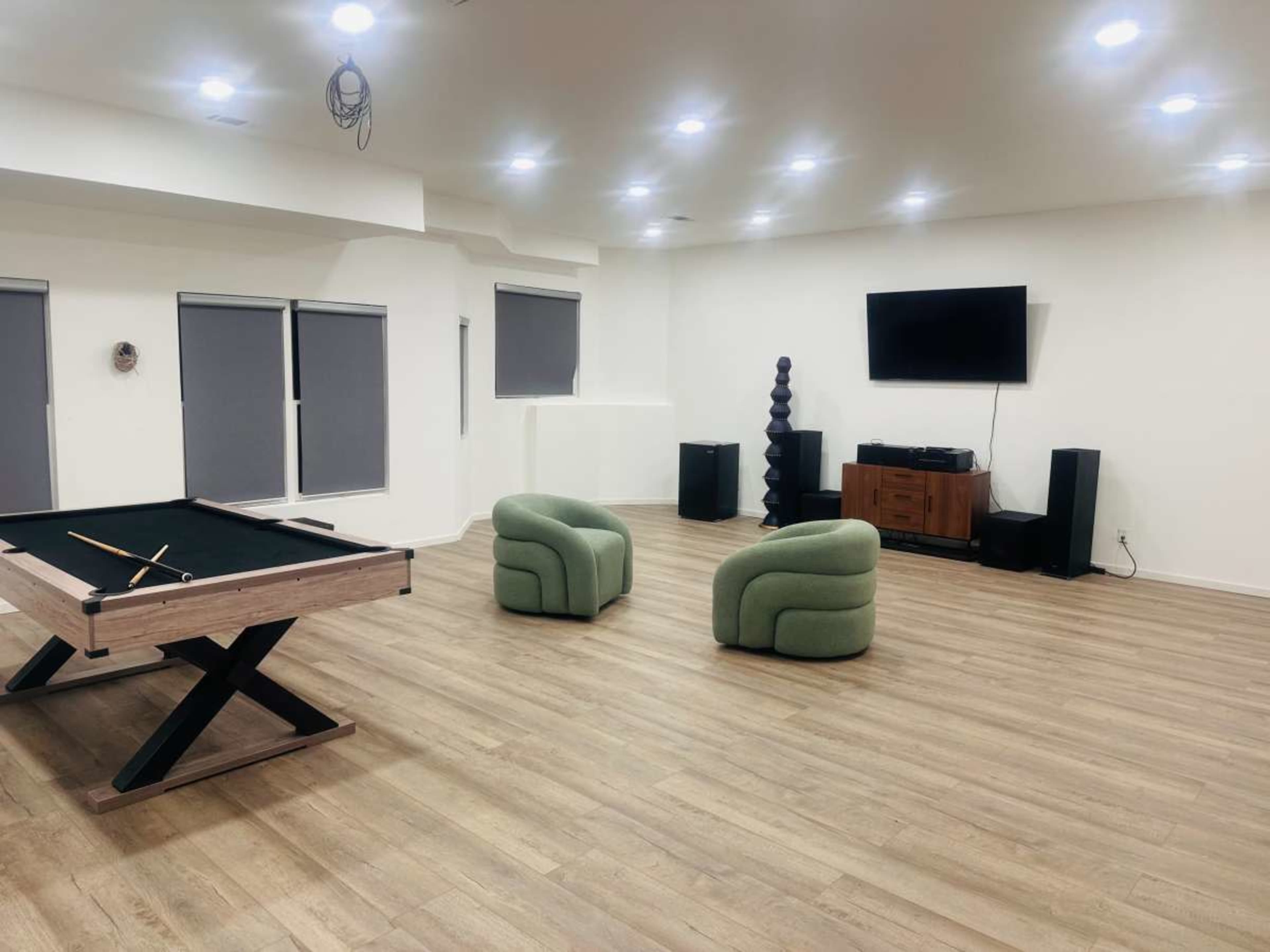 The image shows a spacious room with a pool table, two green armchairs, a television on the wall, and wooden flooring.