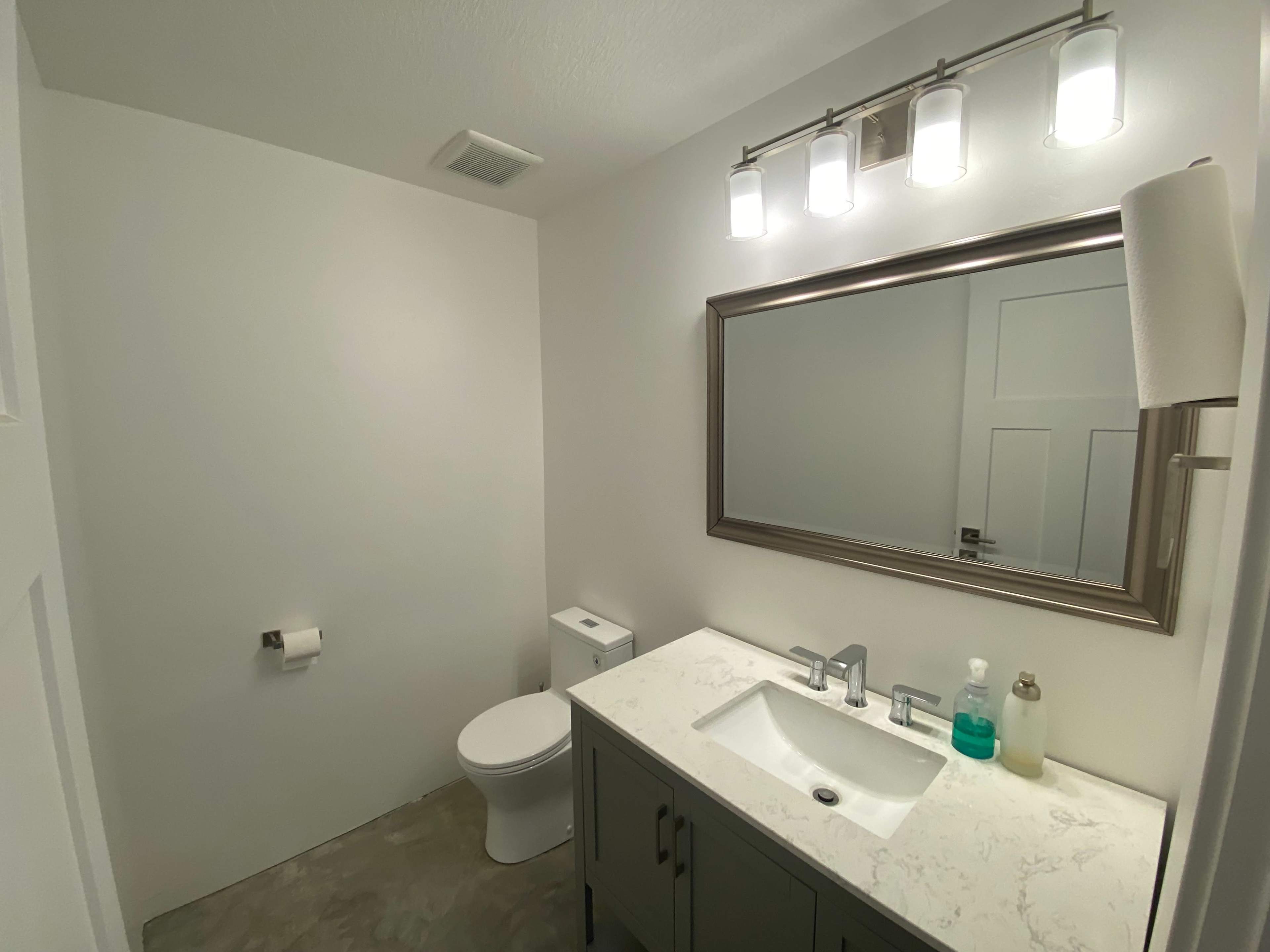 A modern bathroom featuring a toilet, sink with a marble countertop, a large mirror, and overhead lighting.