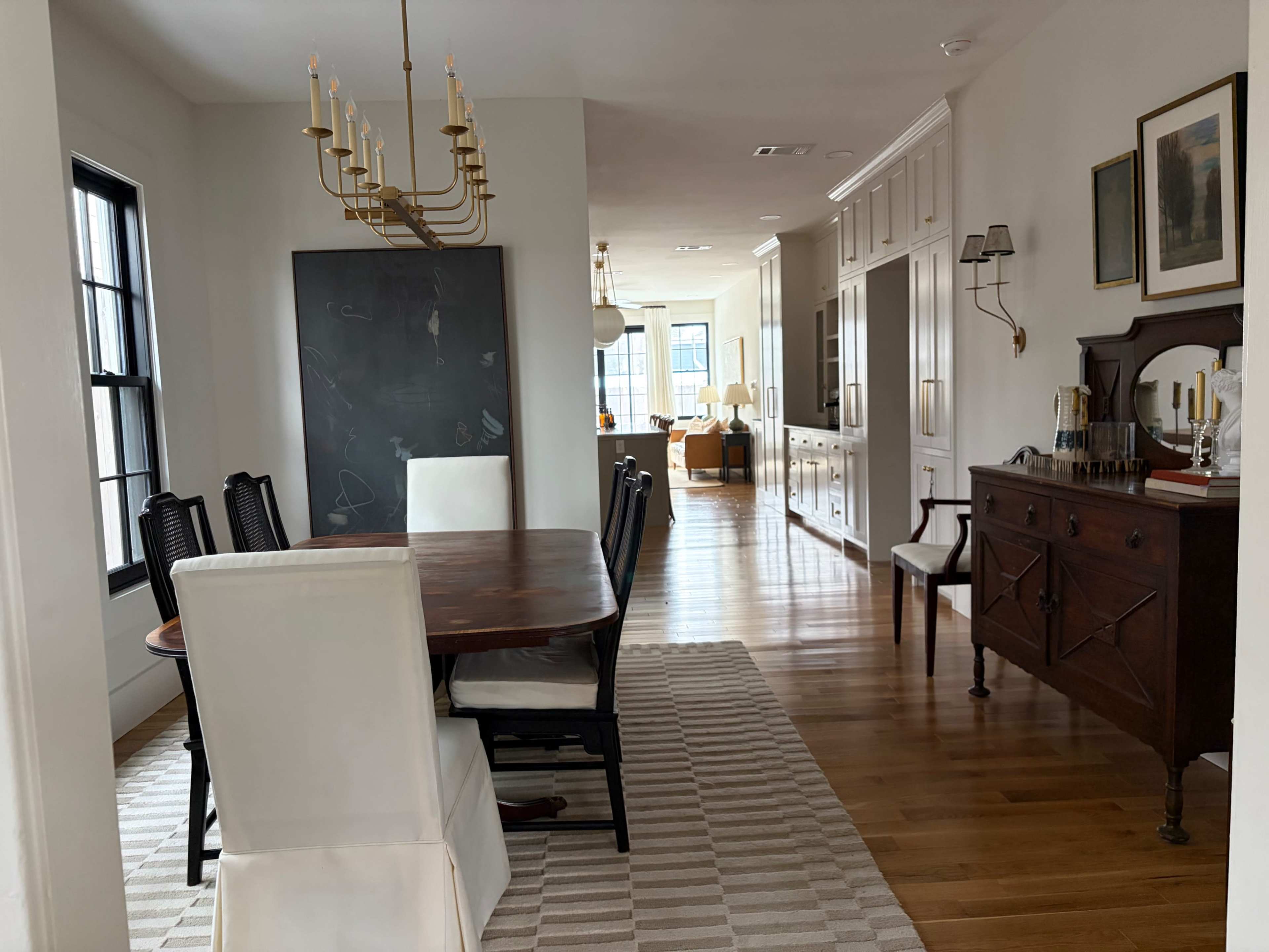 The image shows a dining area with a wooden table and chairs, leading into a hallway with light-colored walls and furnishings.