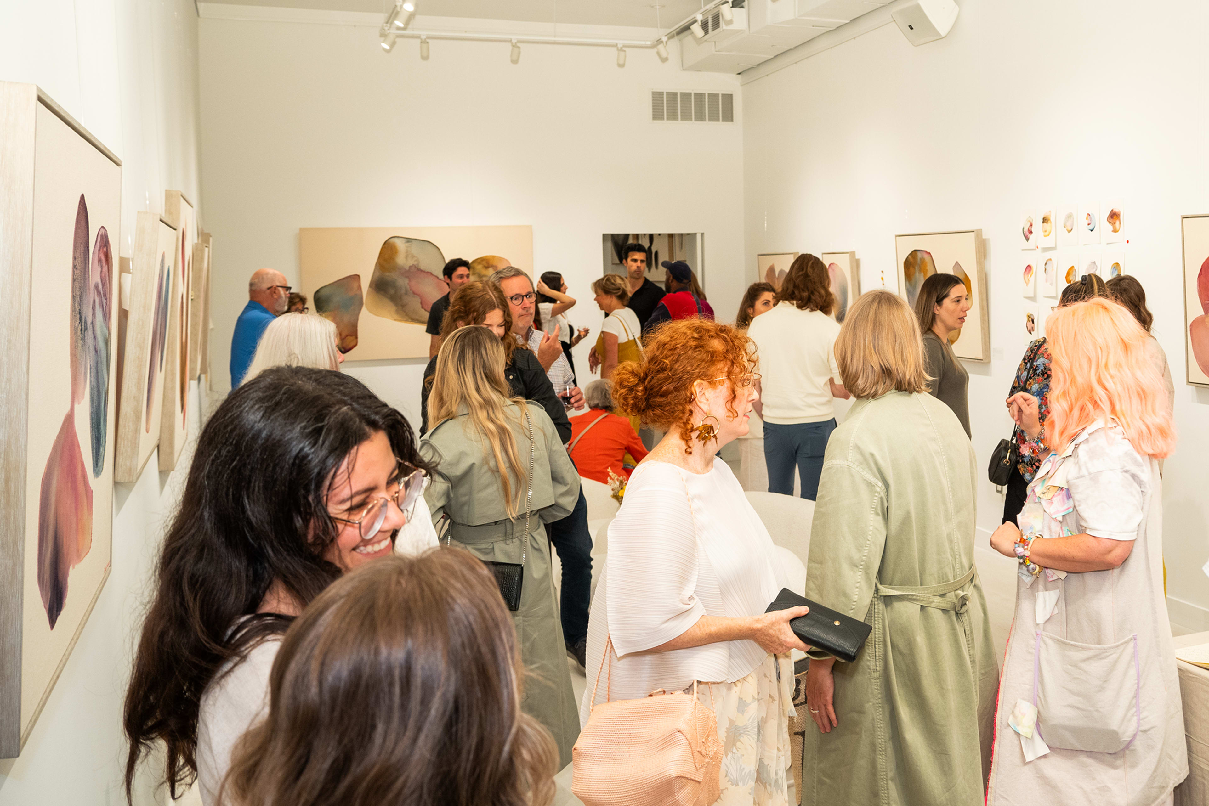A diverse group of people gather in an art gallery, observing various pieces on the walls.