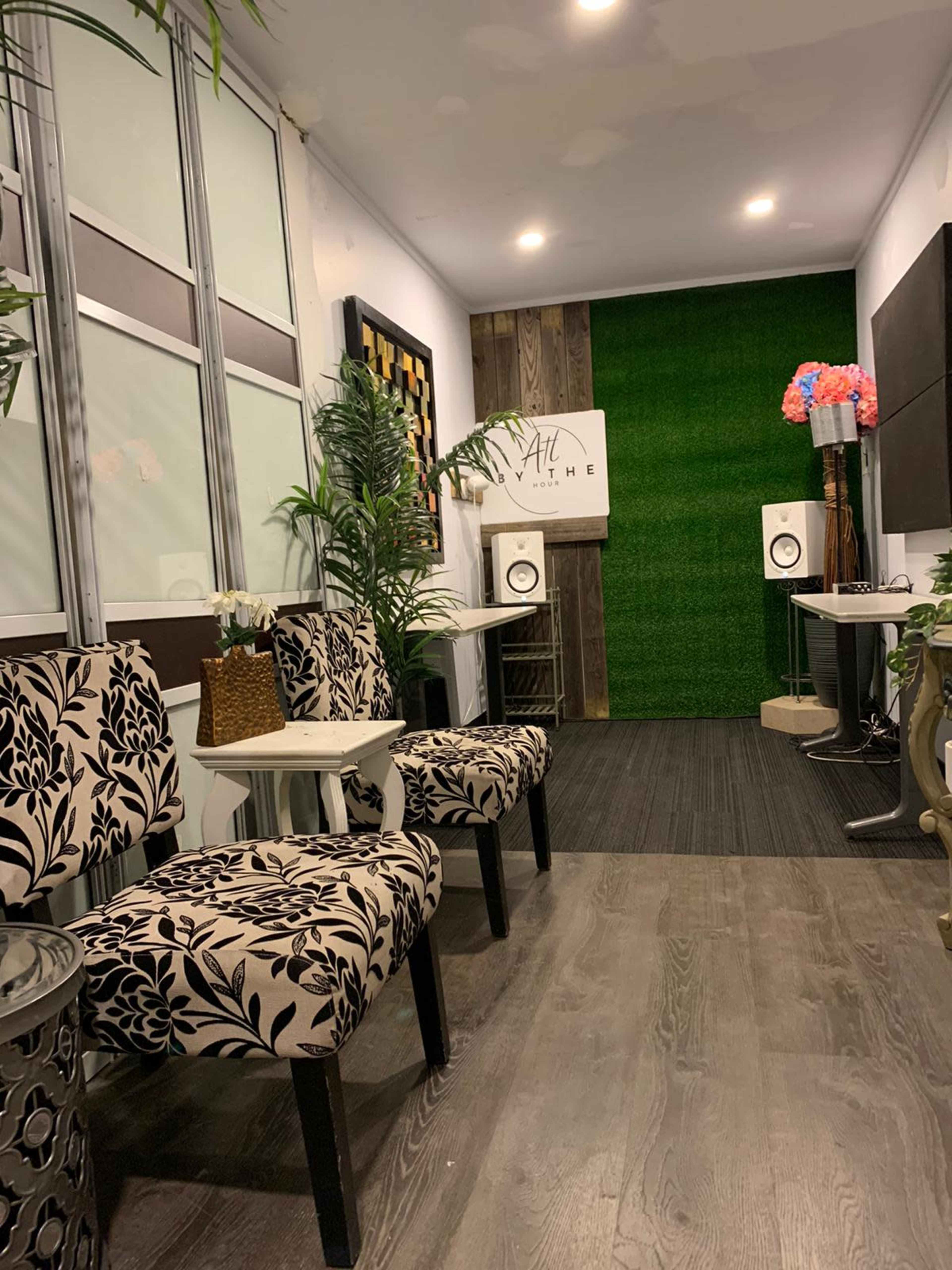 A small waiting area with patterned chairs, potted plants, and speakers against a green wall.