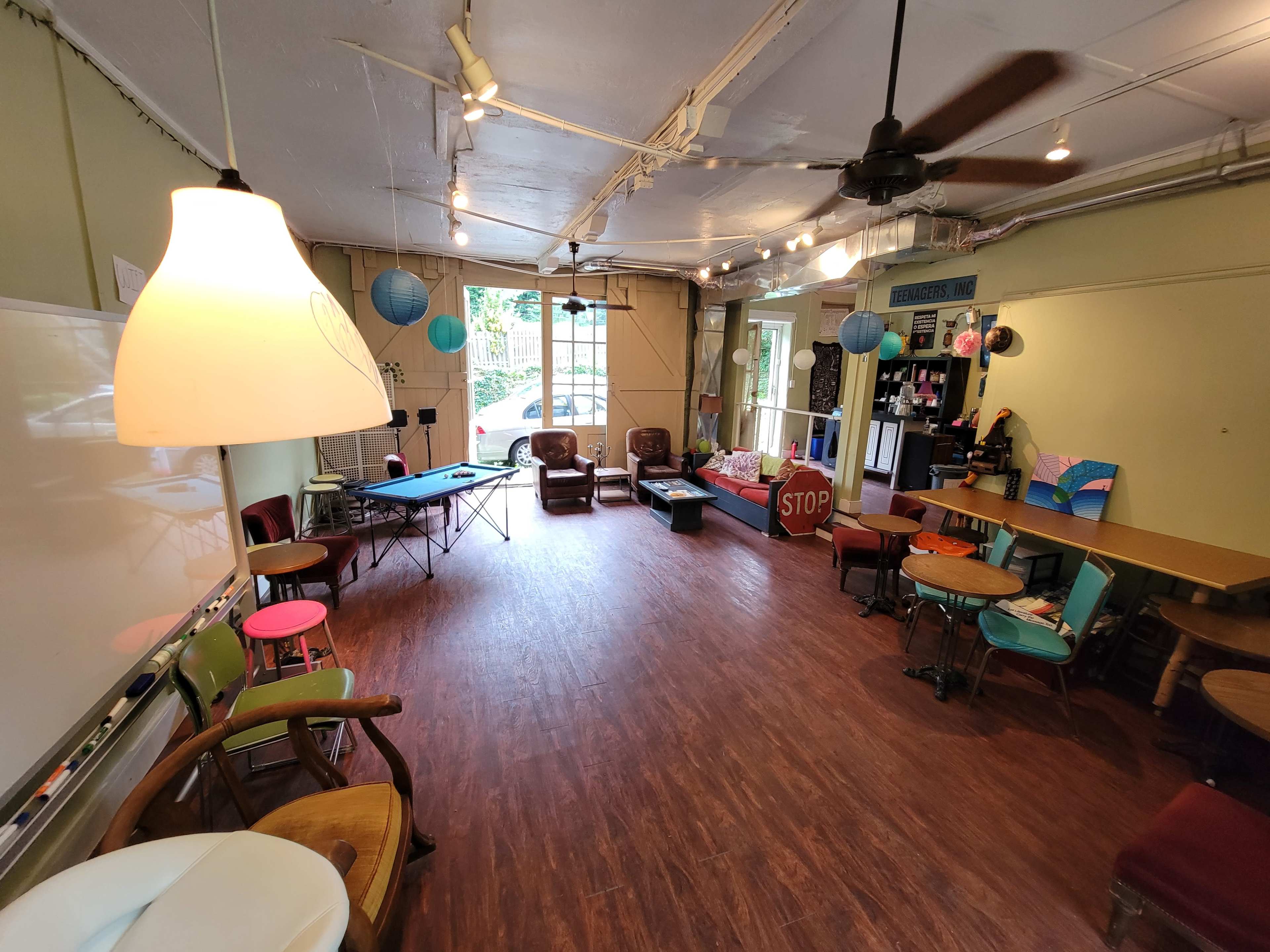 The image shows a spacious, well-lit room furnished with various chairs, tables, and a large window.