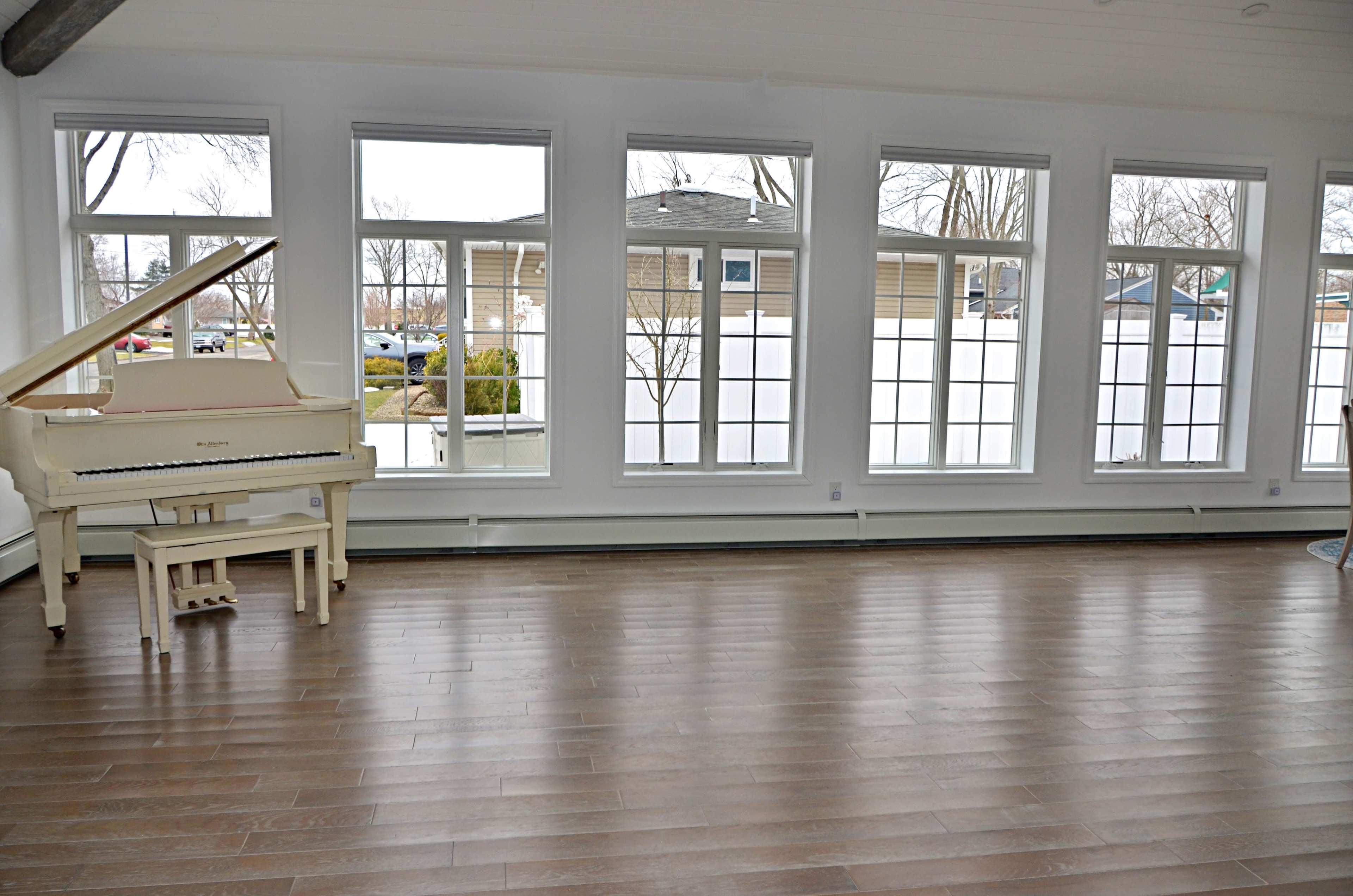 A grand piano is positioned in a spacious room with large windows offering a view of the outdoors.