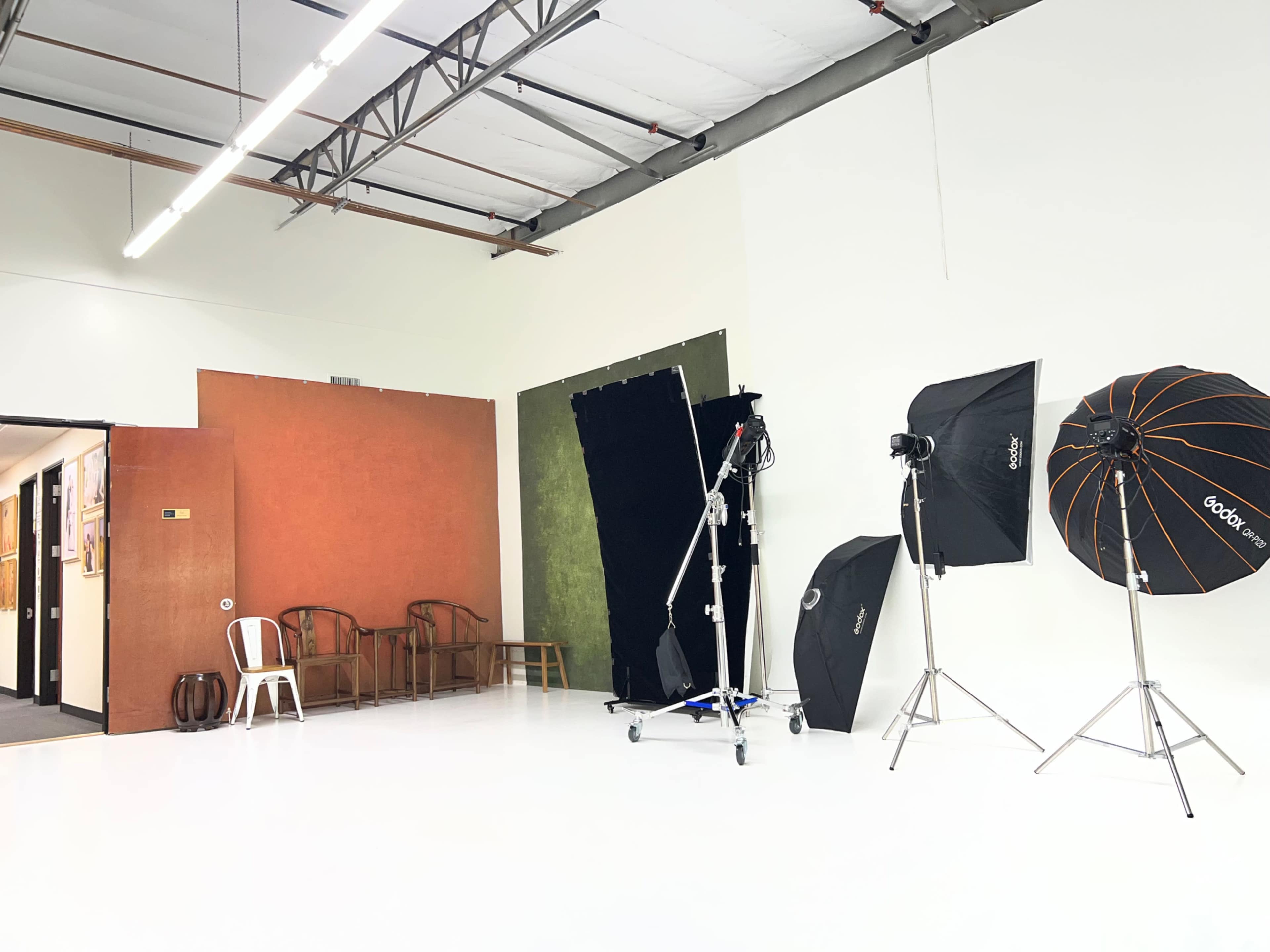 The image shows a photography studio with a white floor, multiple light setups, and a partition featuring textured backgrounds.