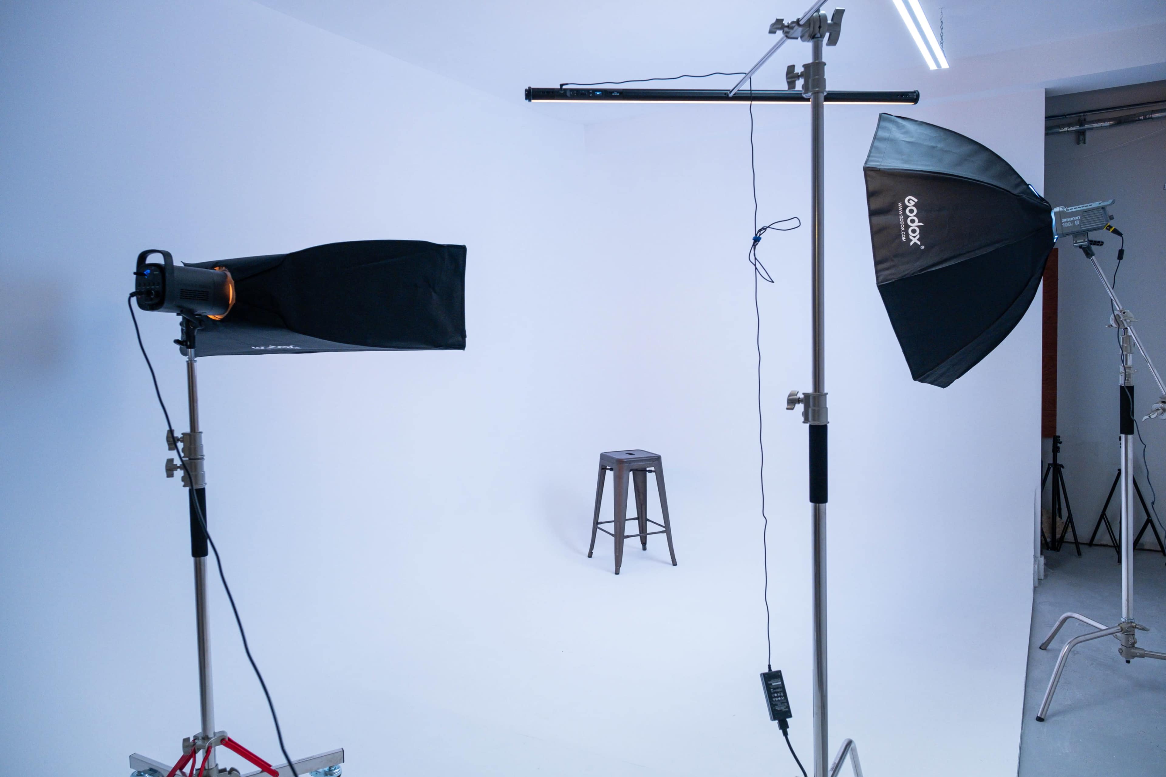 The image shows a photography studio setup with two flash lights and a stool against a white backdrop.